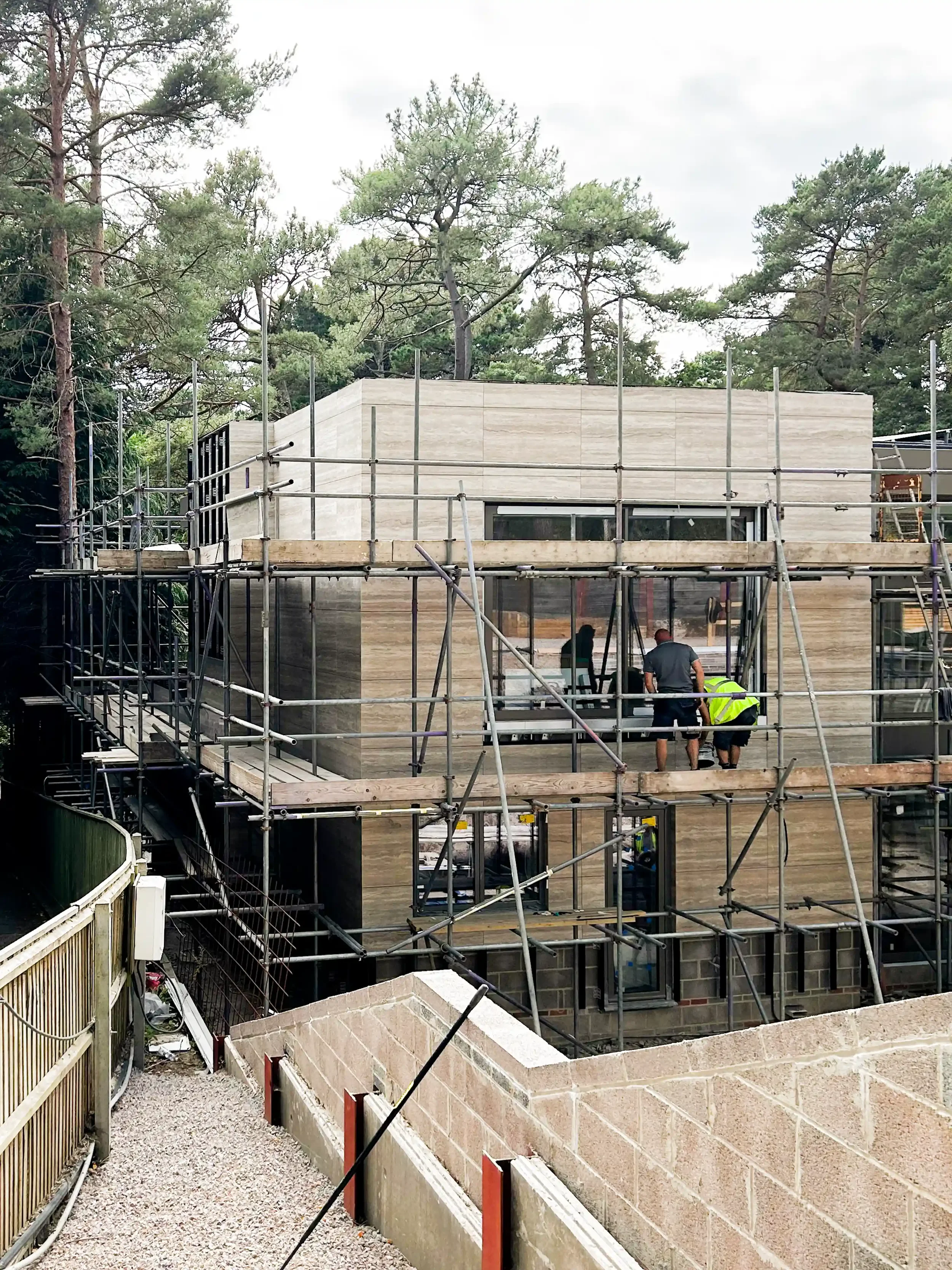 Contemporary residential project under construction showcasing a ventilated facade system cladded with large-format travertine-effect porcelain slabs, surrounded by structural scaffolding.