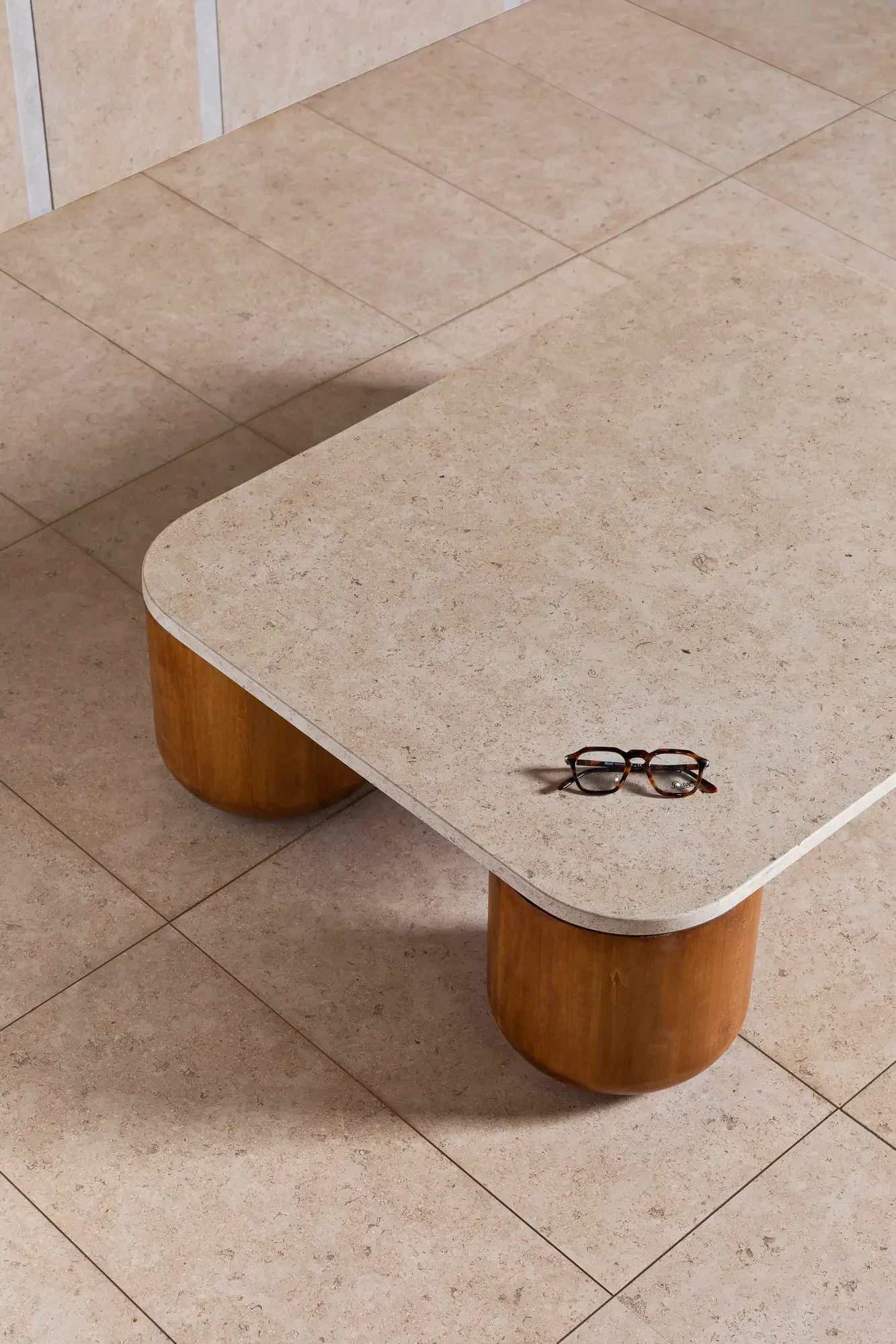 The Luce Di Carrara Porto coffee table, distinguished by its thick, rounded light stone top and cylindrical solid oak wood legs, available through PietraCasa.