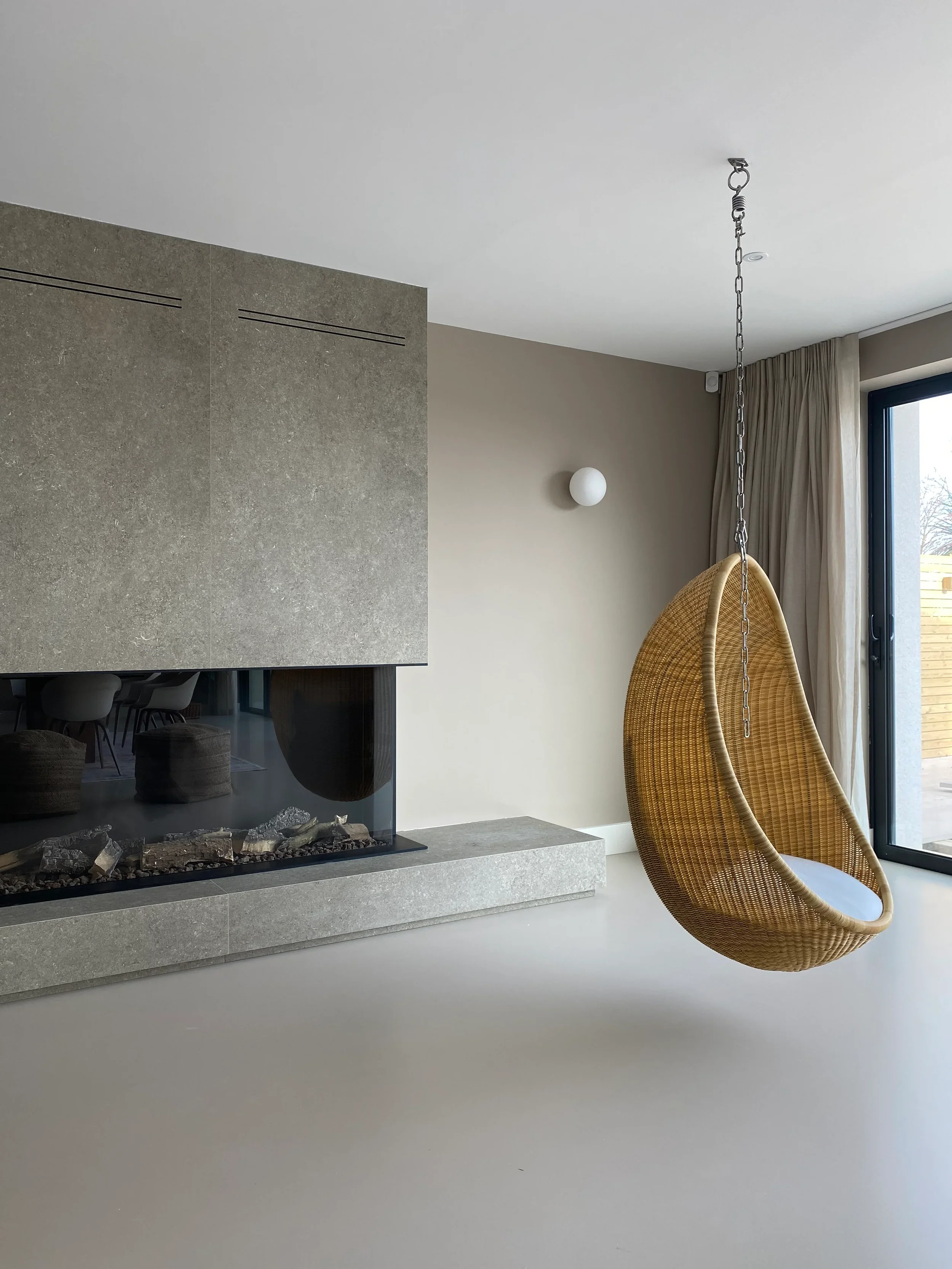 A luxury contemporary living space showcasing a towering chimney breast and low-profile plinth hearth custom-fabricated from large-format stone-effect porcelain slabs, integrated with a three-sided glass gas fireplace.