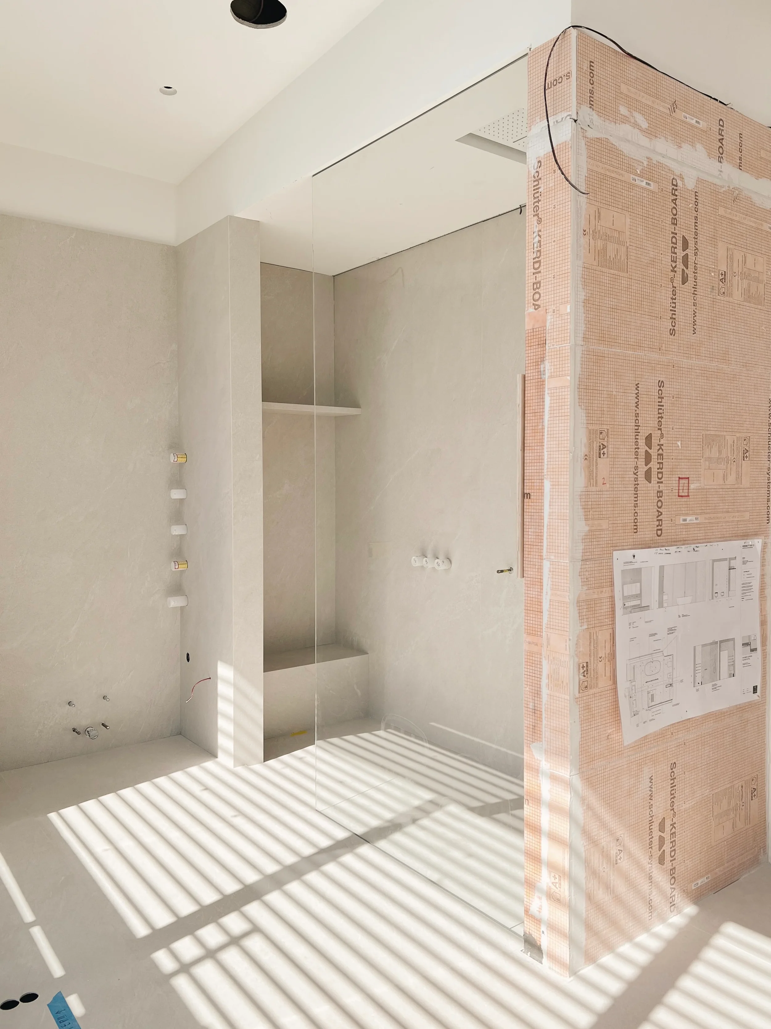 Installation of Inalco Pacific Blanco porcelain tiles and Schluter waterproofing components in a modern wetroom.