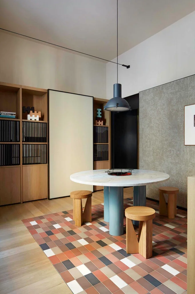 Dining area inside the Casa Mutina Milano showroom, featuring a checkerboard rug effect created with Mutina Rombini ceramic tiles and a round marble-topped table, designed by Studio Urquiola and available through PietraCasa.