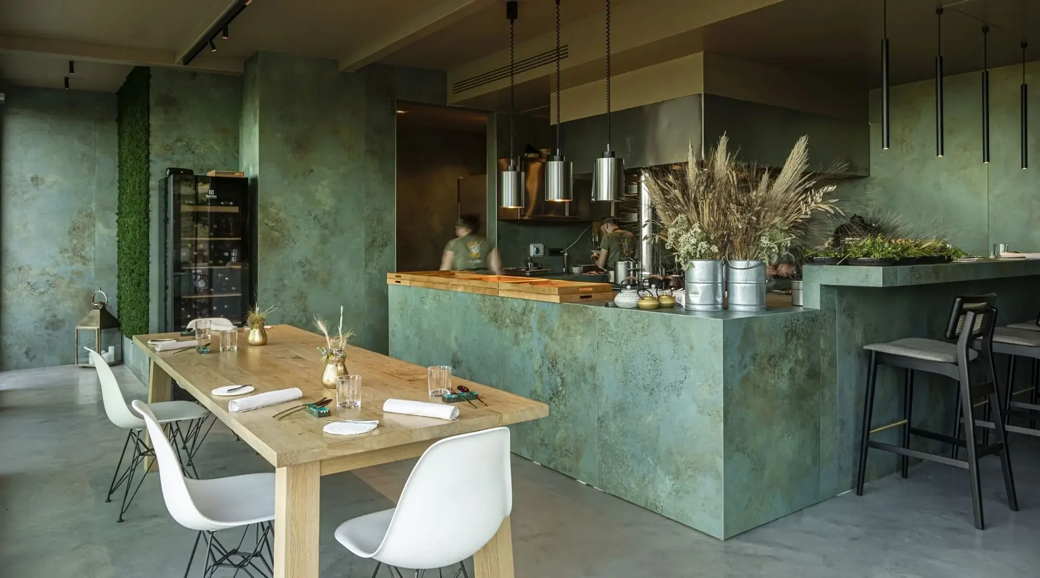 A restaurant interior featuring walls and a large, central island bar clad in Laminam Ossido Verderame, an oxidized copper-effect porcelain slab, available through PietraCasa.