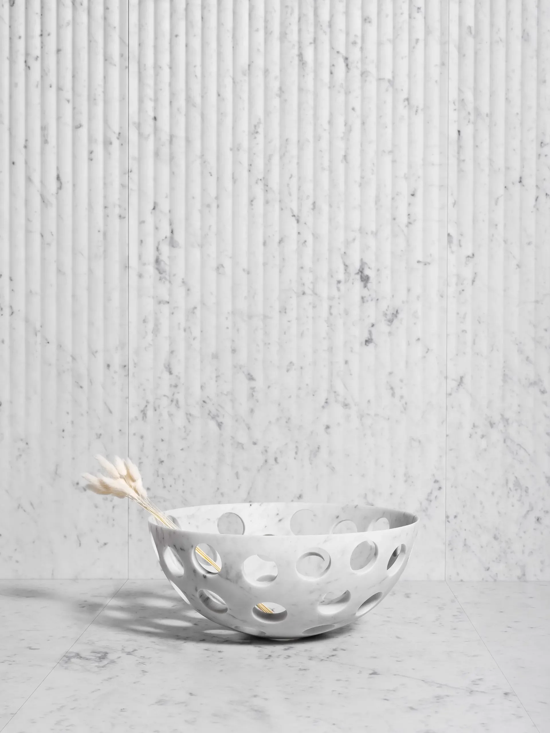 The 'Perforation' pierced marble bowl by Luce di Carrara, showcased against 'Cannette' fluted marble wall panels and a Mali Marble surface, available through PietraCasa.