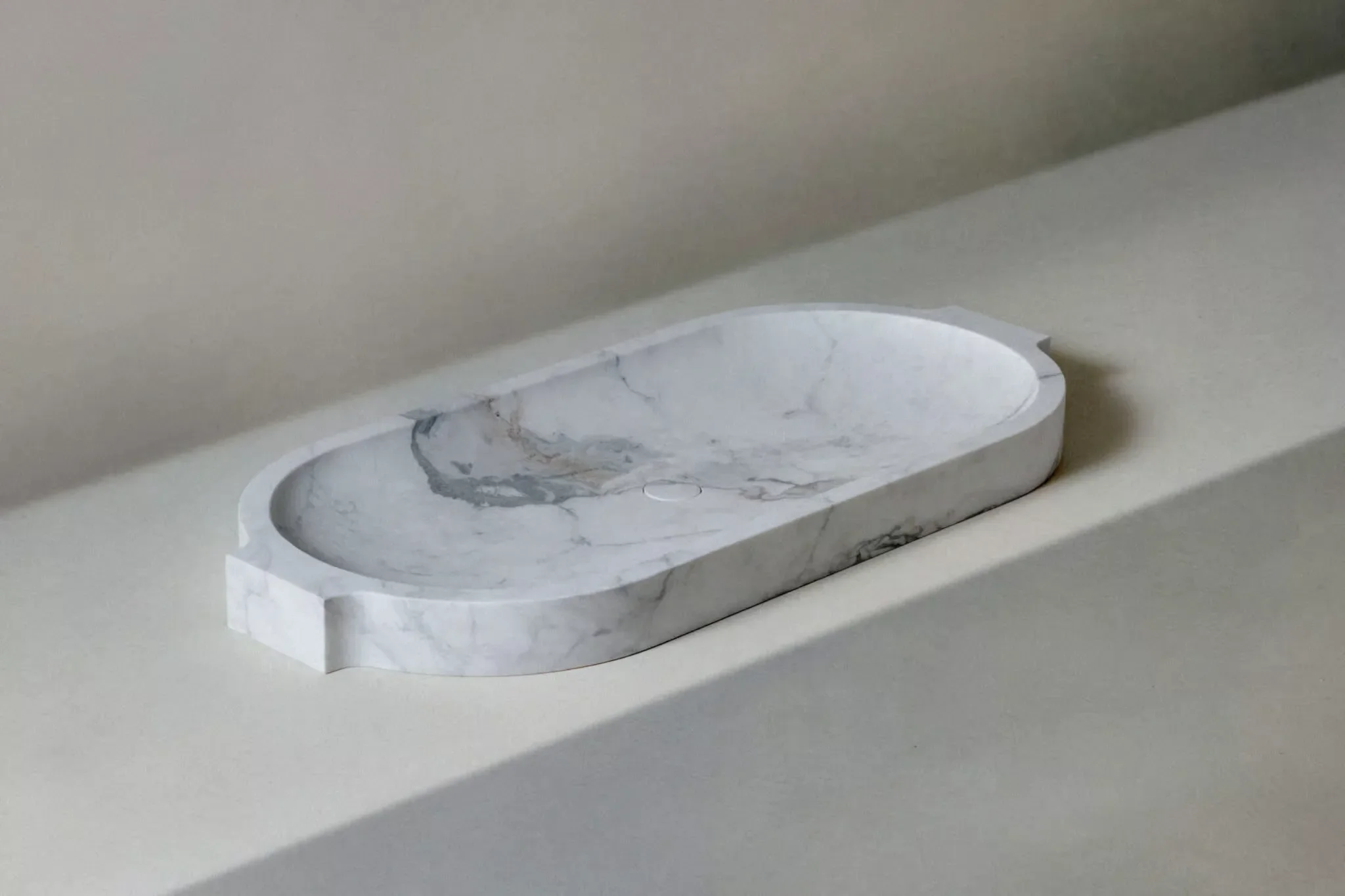 The Silk countertop sink by Kreoo, a luxury washbasin carved from a single block of natural marble featuring a sleek, elongated shape with distinct tabs, available through PietraCasa.