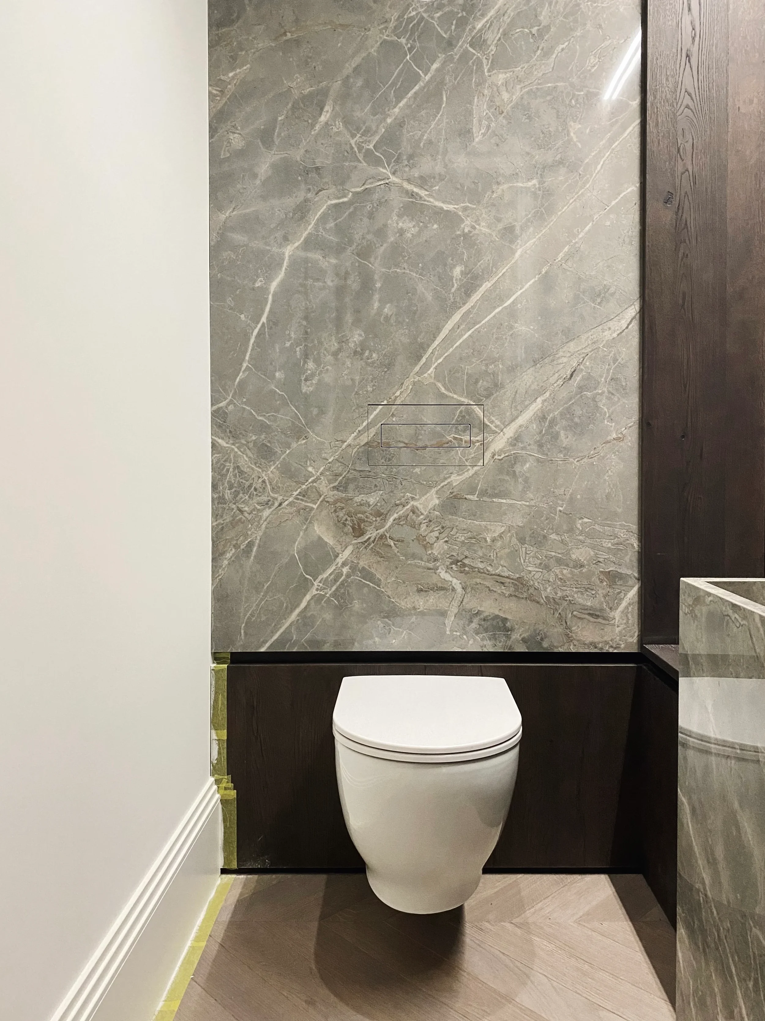 Modern toilet installation with dark wood panelling and a marble-effect porcelain slab feature wall