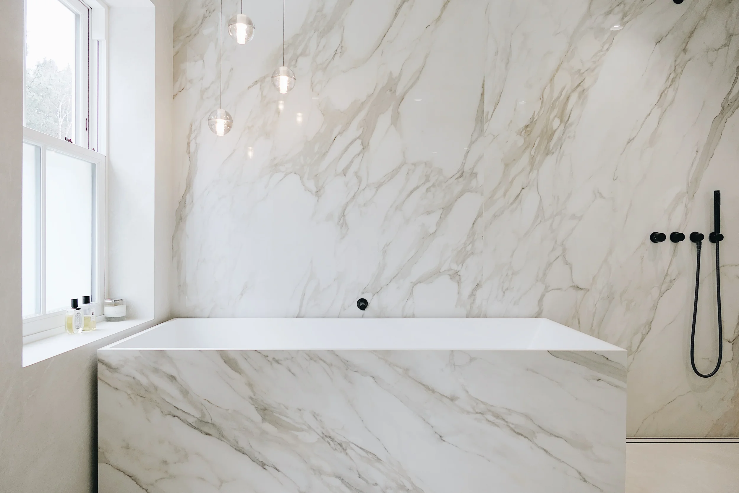 A luxurious master bathroom featuring seamless, large-format marble-effect porcelain cladding on the wall and bath surround, creating a sophisticated and continuous aesthetic.