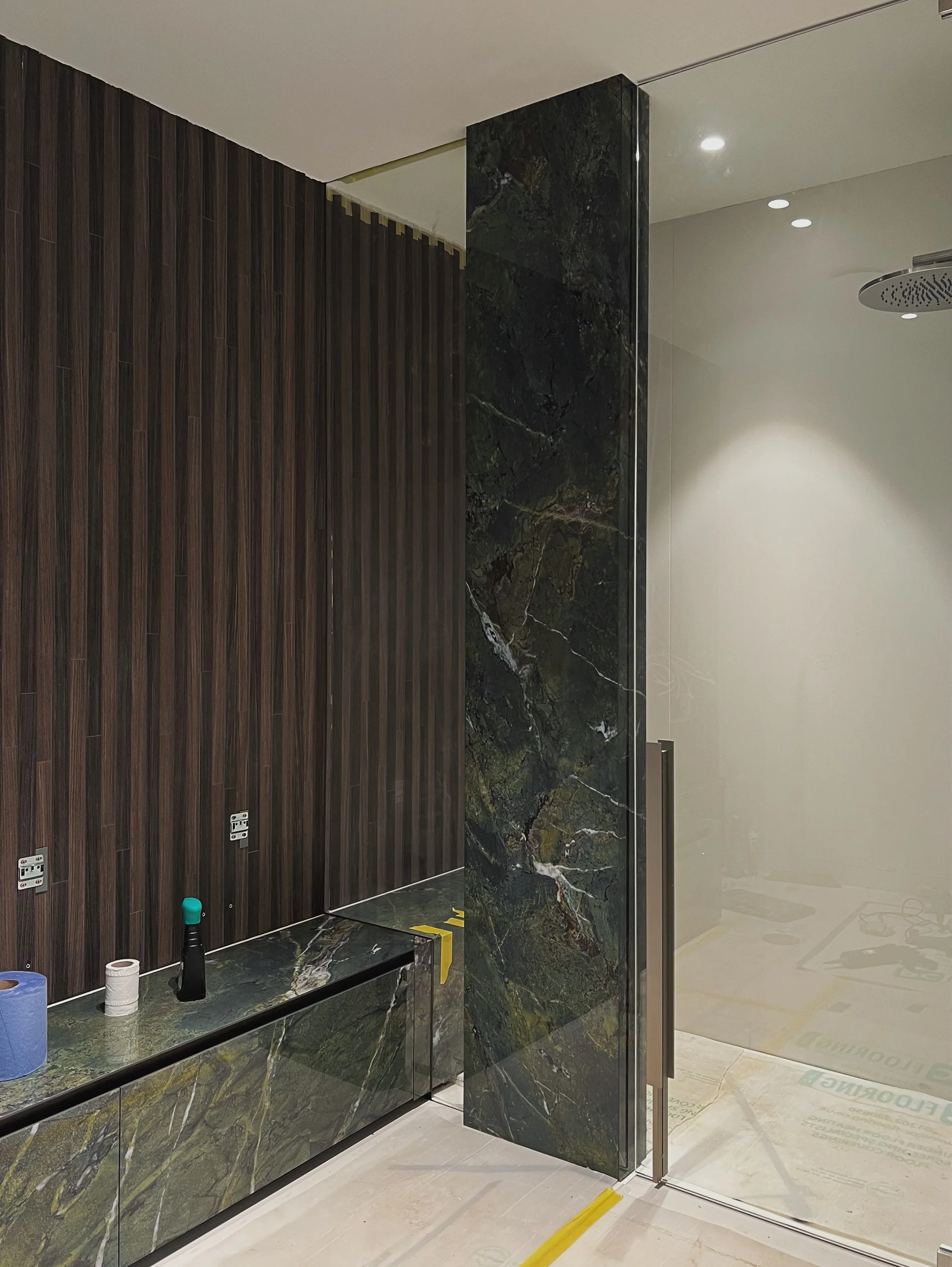Bespoke-fabricated interior featuring dark green marble-effect porcelain cladding on a structural pillar and vanity unit, contrasted with vertical wood-slat wall paneling.