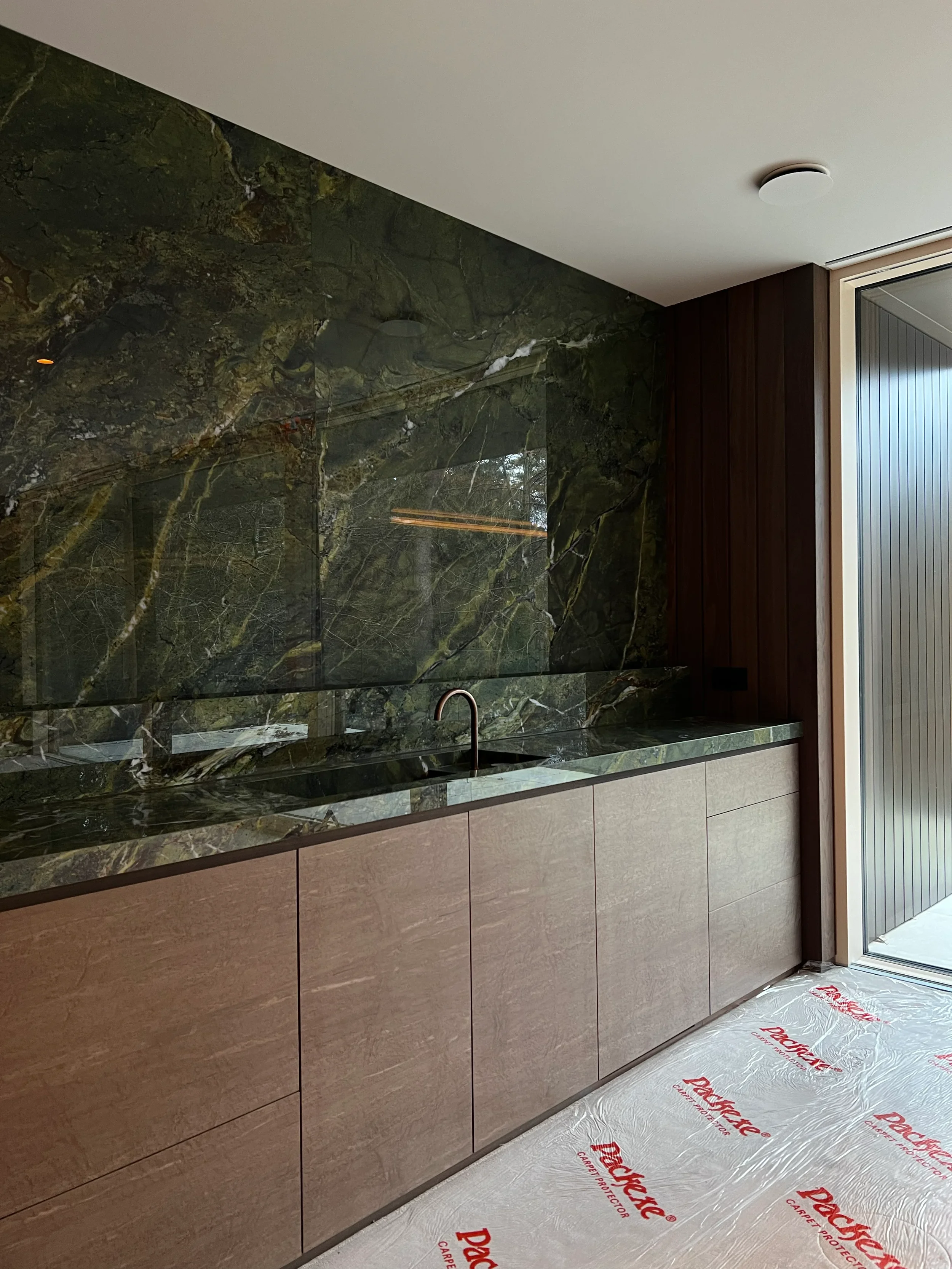 A luxury kitchen installation featuring a striking bookmatched emerald green marble-effect porcelain splashback and matching polished worktop by PietraCasa.