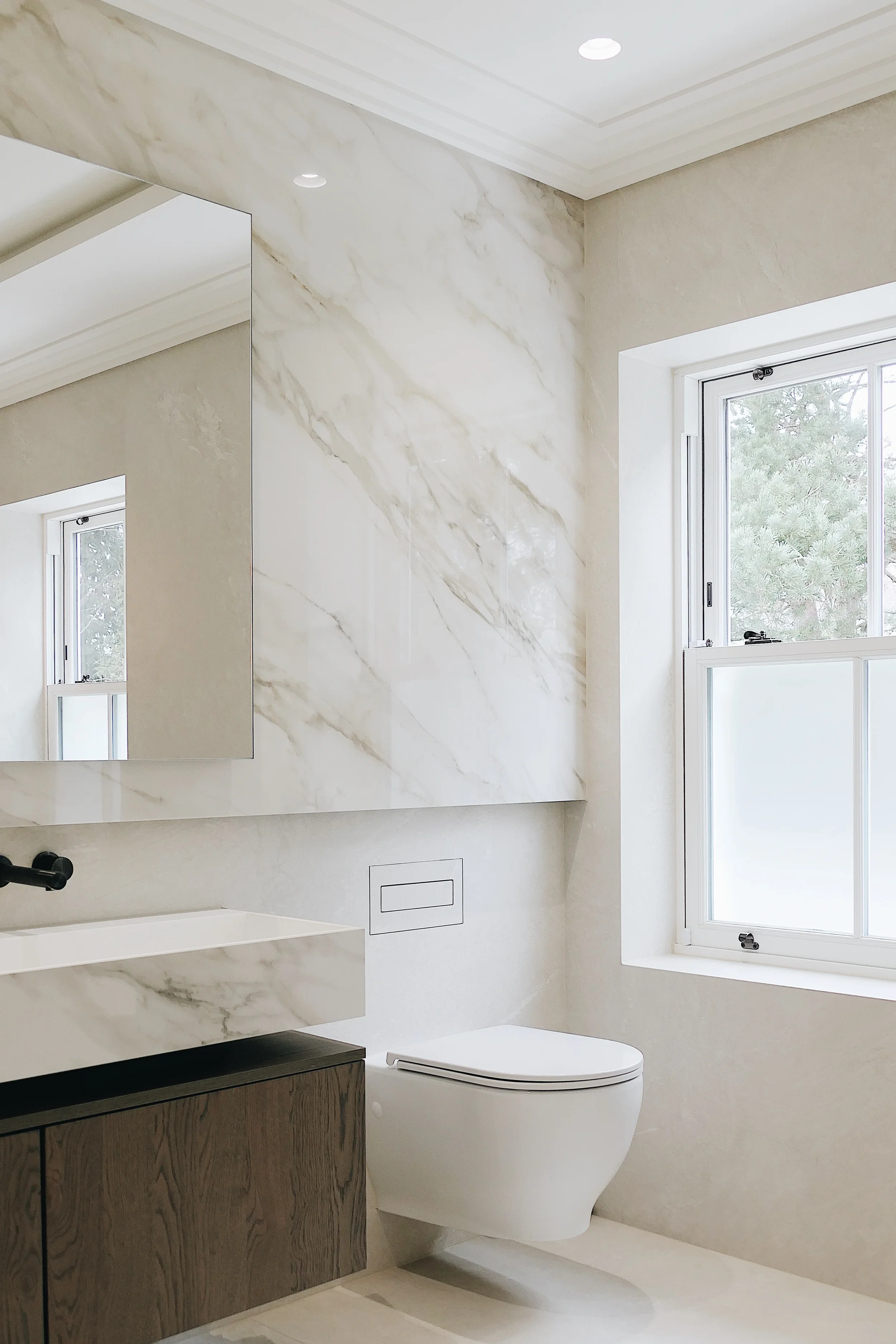 A luxurious modern bathroom featuring seamless, large-format marble-effect porcelain wall cladding and vanity, creating a sophisticated and continuous aesthetic.