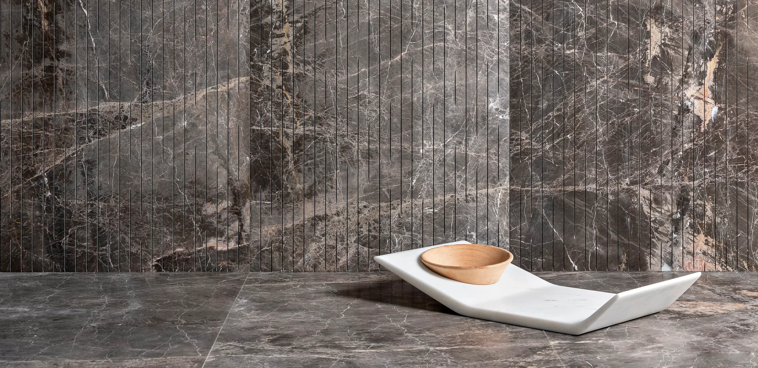 Luce di Carrara marble surfaces featuring a large-format grey marble floor combined with a uniquely grooved, vertically-slatted marble wall, available through PietraCasa.
