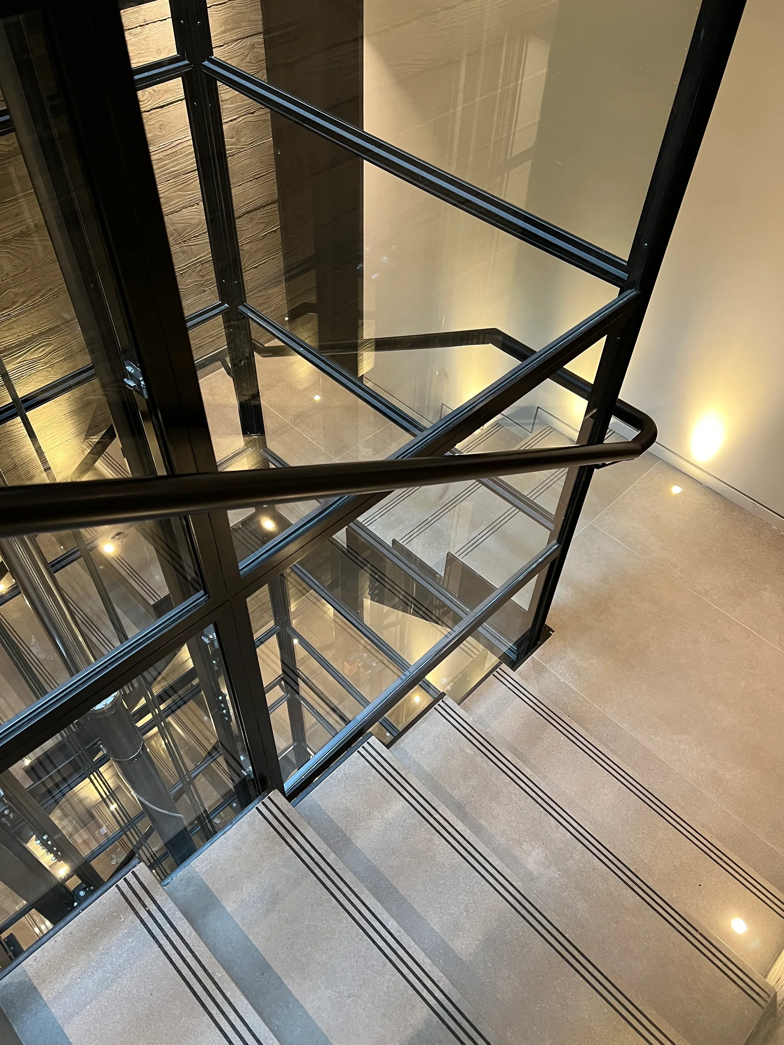 Modern porcelain slab staircase wrapping around a black steel-framed glass elevator.