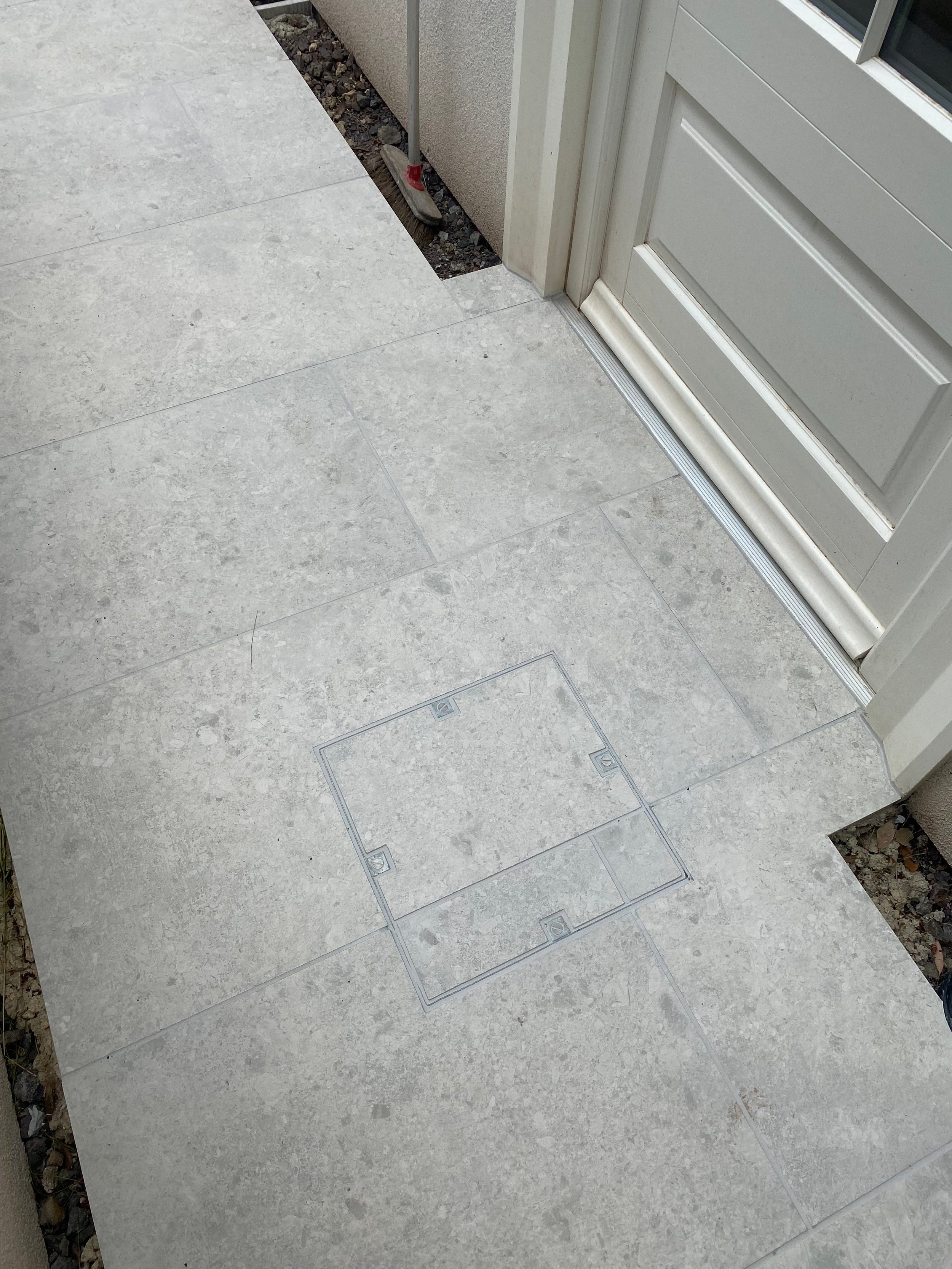 Close-up view of precision-fitted porcelain paving tiles featuring a discreet, integrated recessed manhole cover outside a residential entrance.
