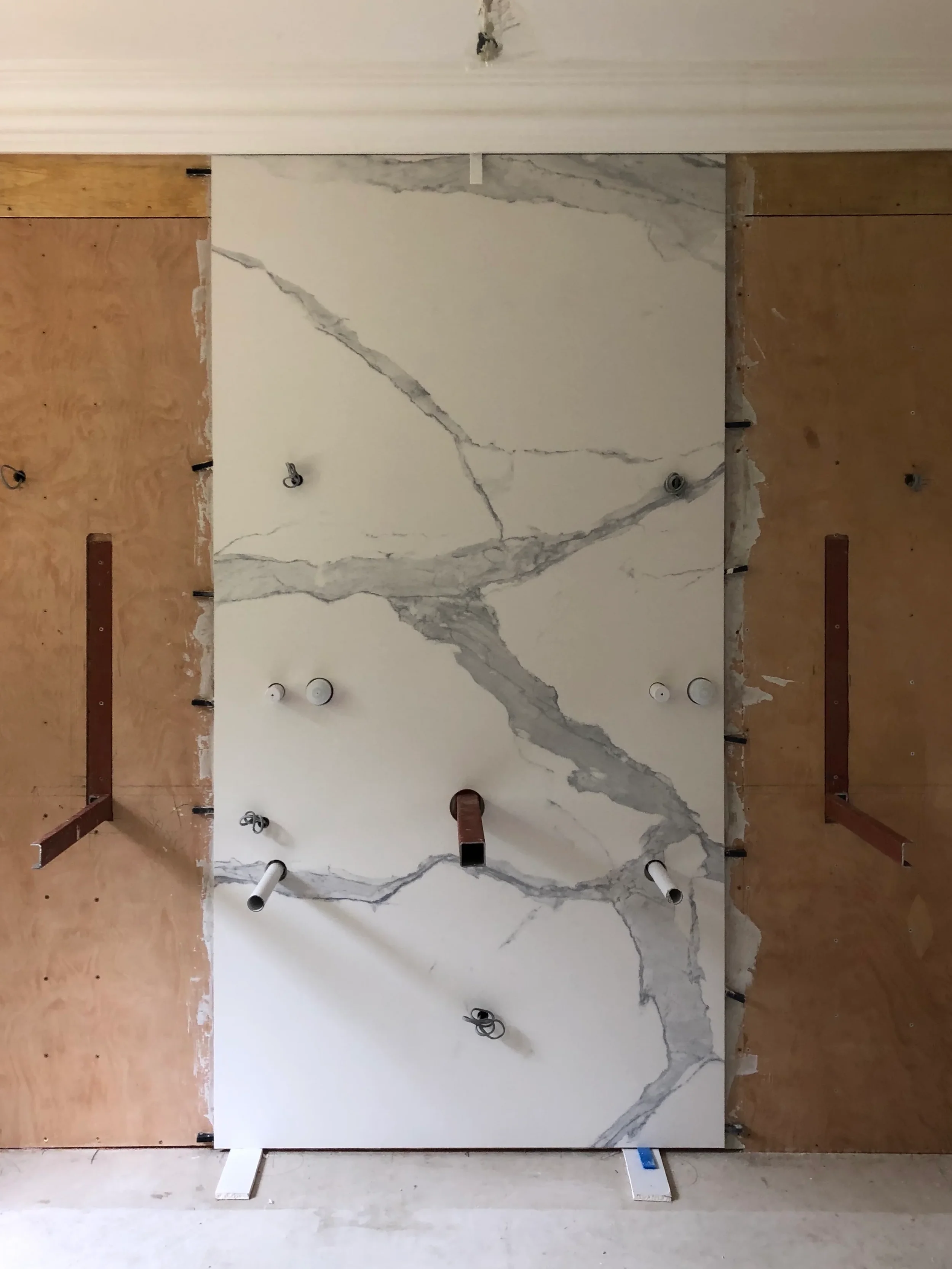 Detailed on-site view of a large-format white Calacatta marble-effect porcelain slab being dry-fitted with precision pipe cutouts onto a reinforced timber frame by PietraCasa.