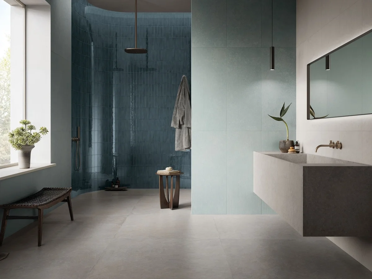 Modern bathroom environment featuring Supergres INX collection concrete-effect porcelain tiles, with an Aqua accent shower wall and lighter Plume and Pearl tones on the main walls, supplied by PietraCasa.