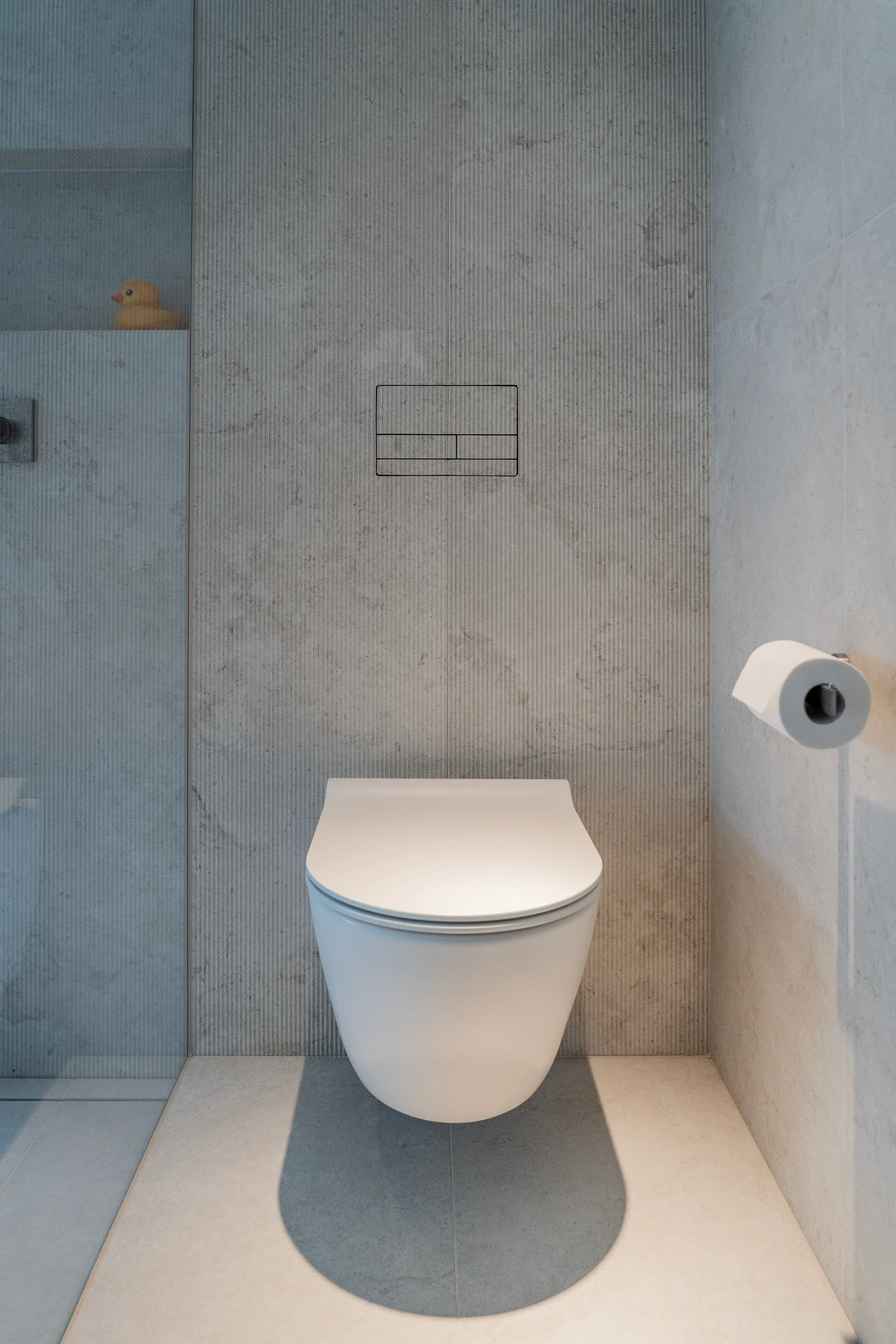 Wall-mounted WC with a sleek, flush-fit Clanea dual-flush plate on textured Living Ceramics Verso Cross Cut porcelain wall tiles by Abitalia and Pietracasa.