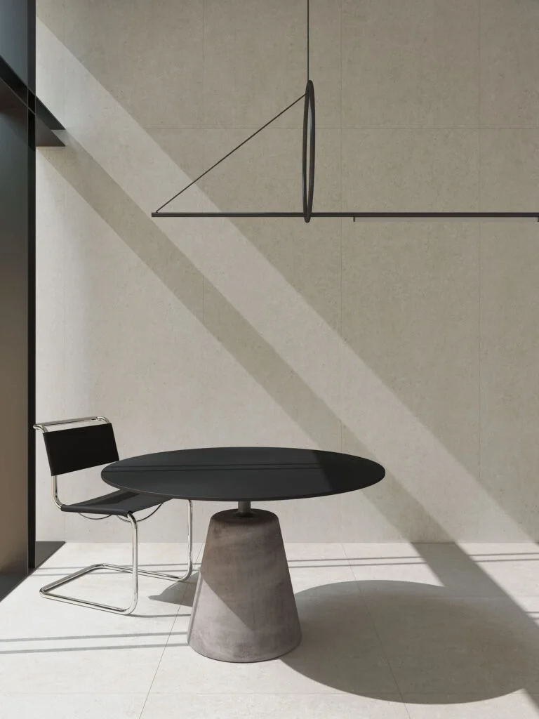 A minimalist dining space featuring Living Ceramics Bera&Beren Light Grey wall and floor tiles, illuminated by the Marset Ihana lighting system, with a sleek pedestal table and the iconic Cesca Chair, available through PietraCasa.