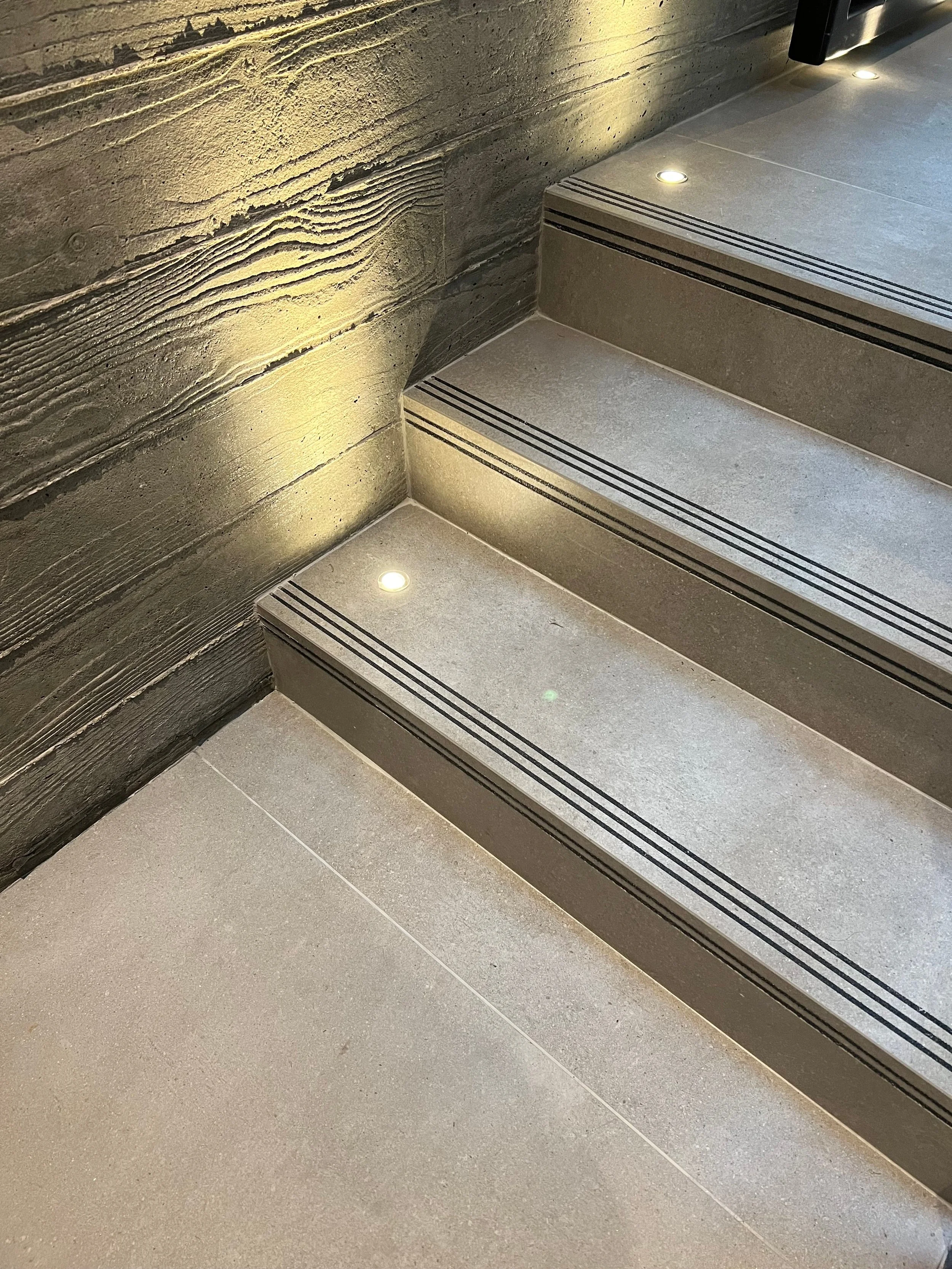 Close-up view of grey porcelain stairs featuring integrated micro LED spotlights and black non-slip safety treads.