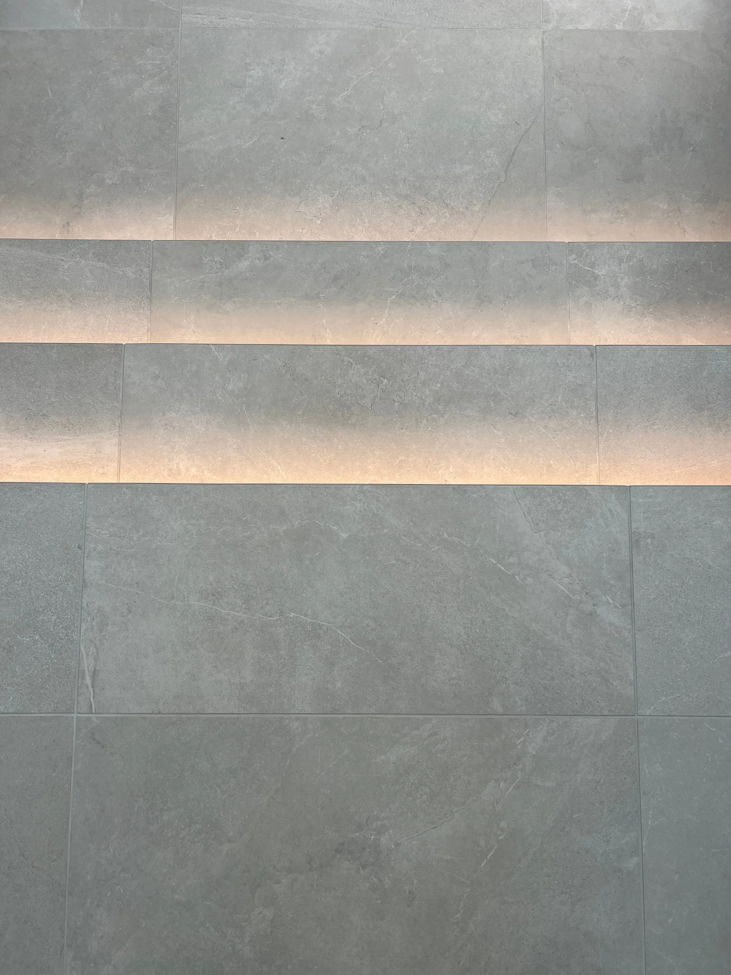 A detailed overhead view of a luxury contemporary staircase featuring custom-fabricated treads from large-format, textured grey stone-effect porcelain tiles, beautifully highlighted by warm, concealed linear LED strip lighting.