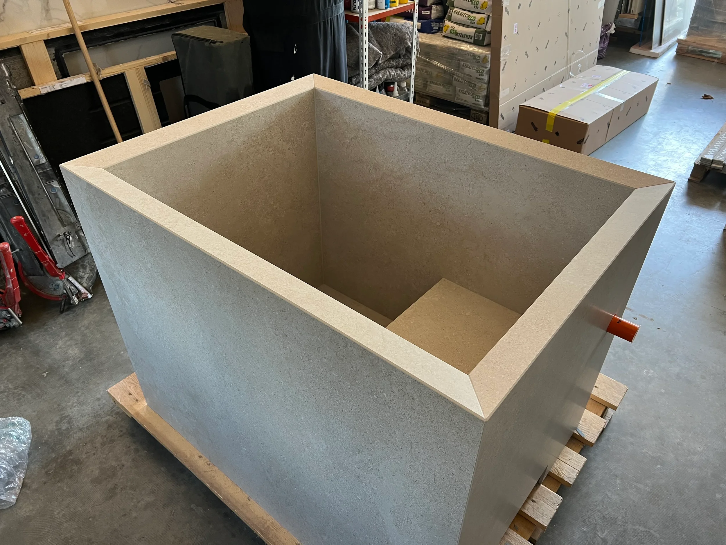 Bespoke freestanding plunge pool custom-fabricated from large-format textured beige porcelain slabs in a workshop.