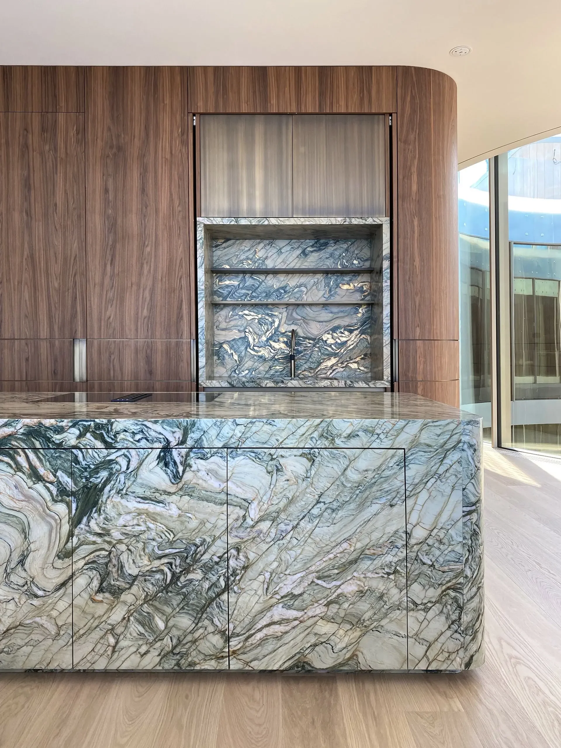 Kitchen island, countertop, and backsplash featuring Fusion Wow Light Brazilian quartzite by Antolini, paired with American black walnut cabinetry, supplied by PietraCasa.