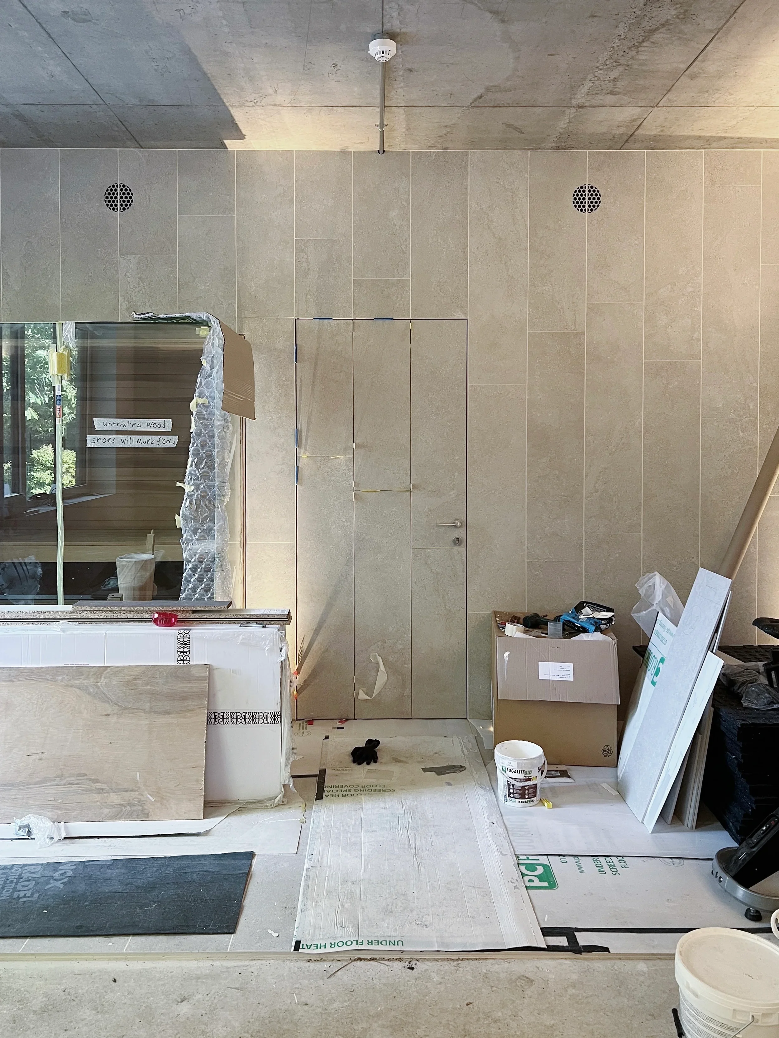 Bespoke hidden door flush-fitted with matching large-format beige porcelain wall tiles in a wellness area.