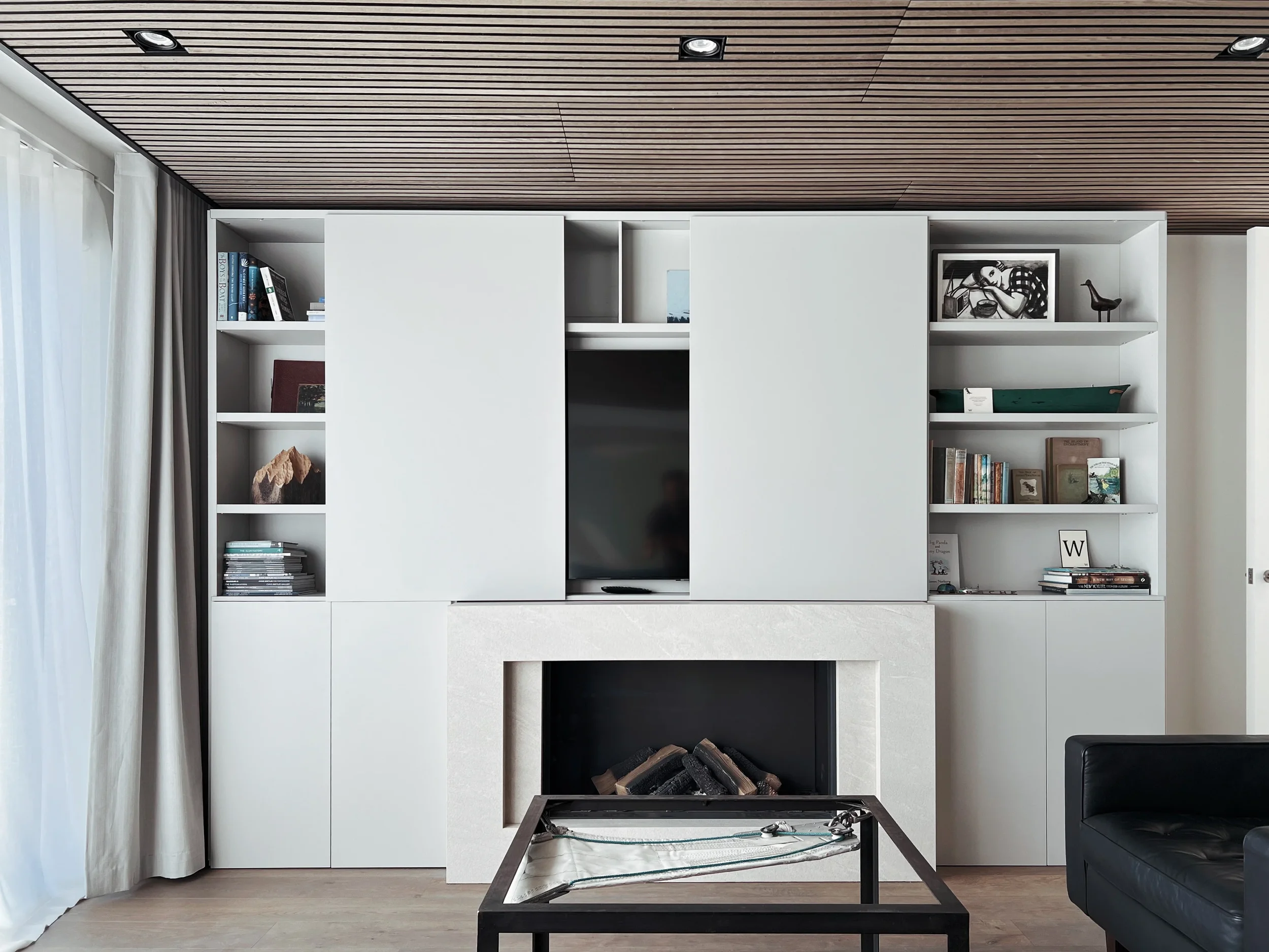 A luxury living room featuring a custom fireplace surround fabricated from Inalco large-format porcelain, seamlessly integrated with a bespoke white minimalist library and media unit.