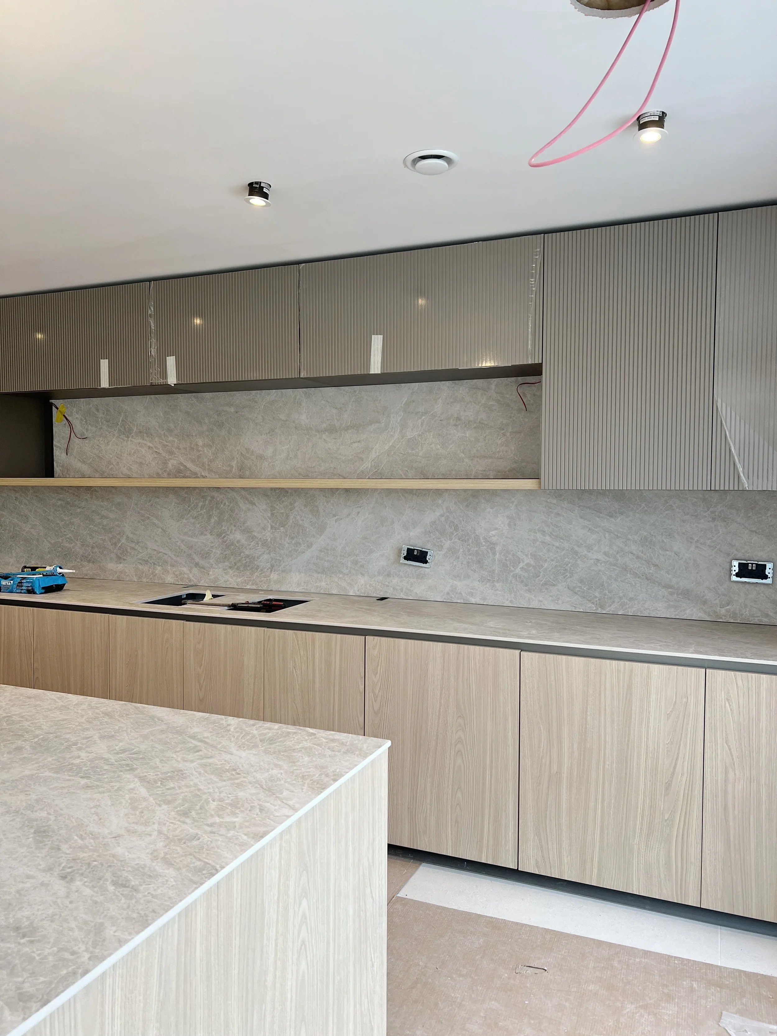 A contemporary kitchen installation featuring seamless, large-format porcelain worktops and a matching full-height splashback, creating a clean and luxurious aesthetic.