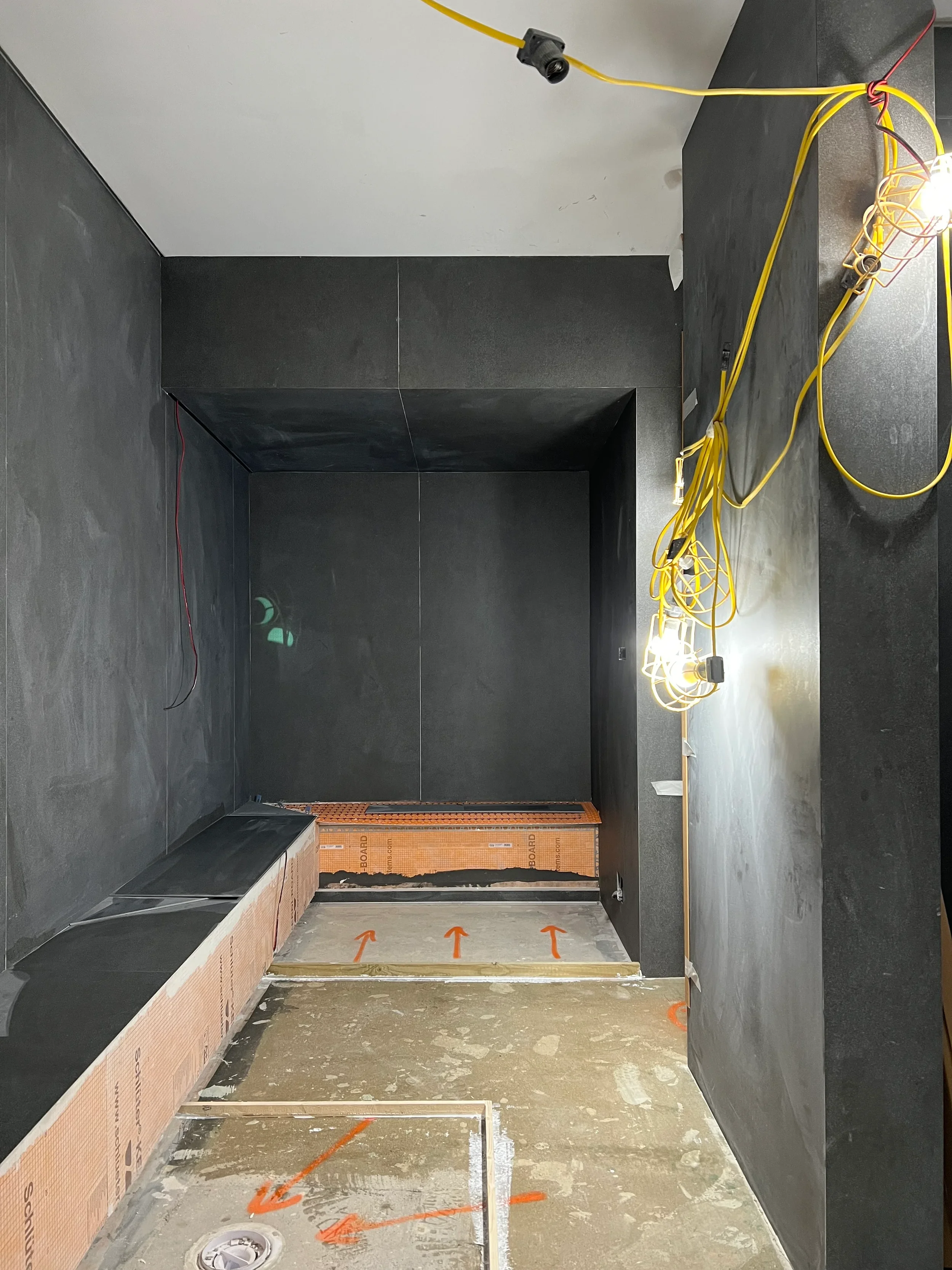 Installation of large-format dark porcelain slabs and Schluter systems in a custom steam room.