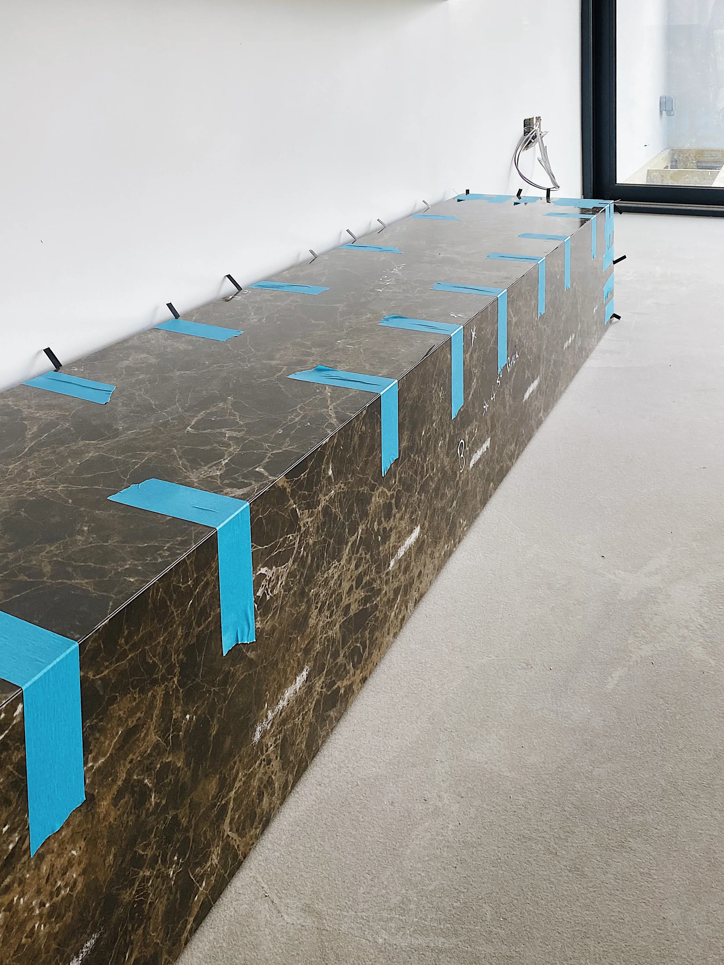 A glimpse into the professional installation process of a bespoke, large-format dark marble-effect porcelain feature, emphasizing the meticulous detail and precision of custom stone-effect work.
