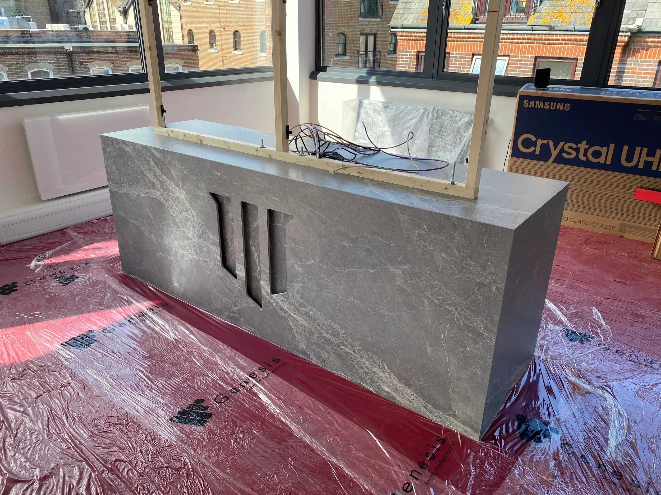 Bespoke-fabricated commercial reception desk featuring grey marble-effect porcelain panels, precision-cut integrated logo detailing, and high-end joinery construction