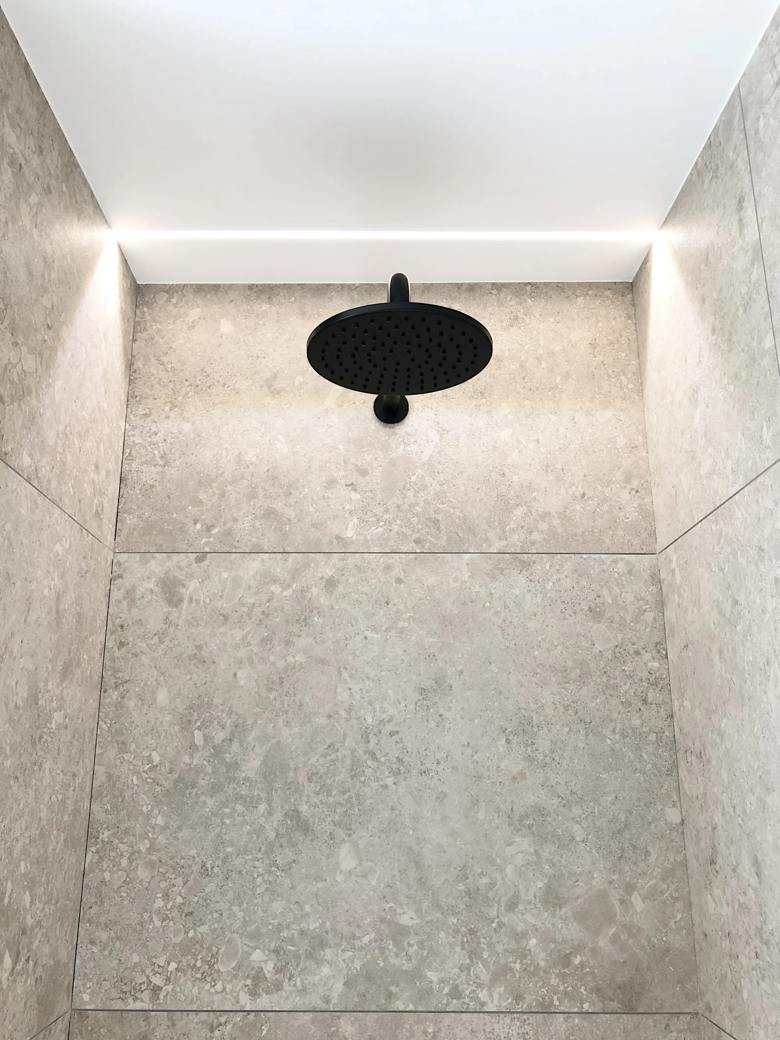 Modern walk-in shower with large-format grey porcelain tiles and a matt black rainfall shower head.