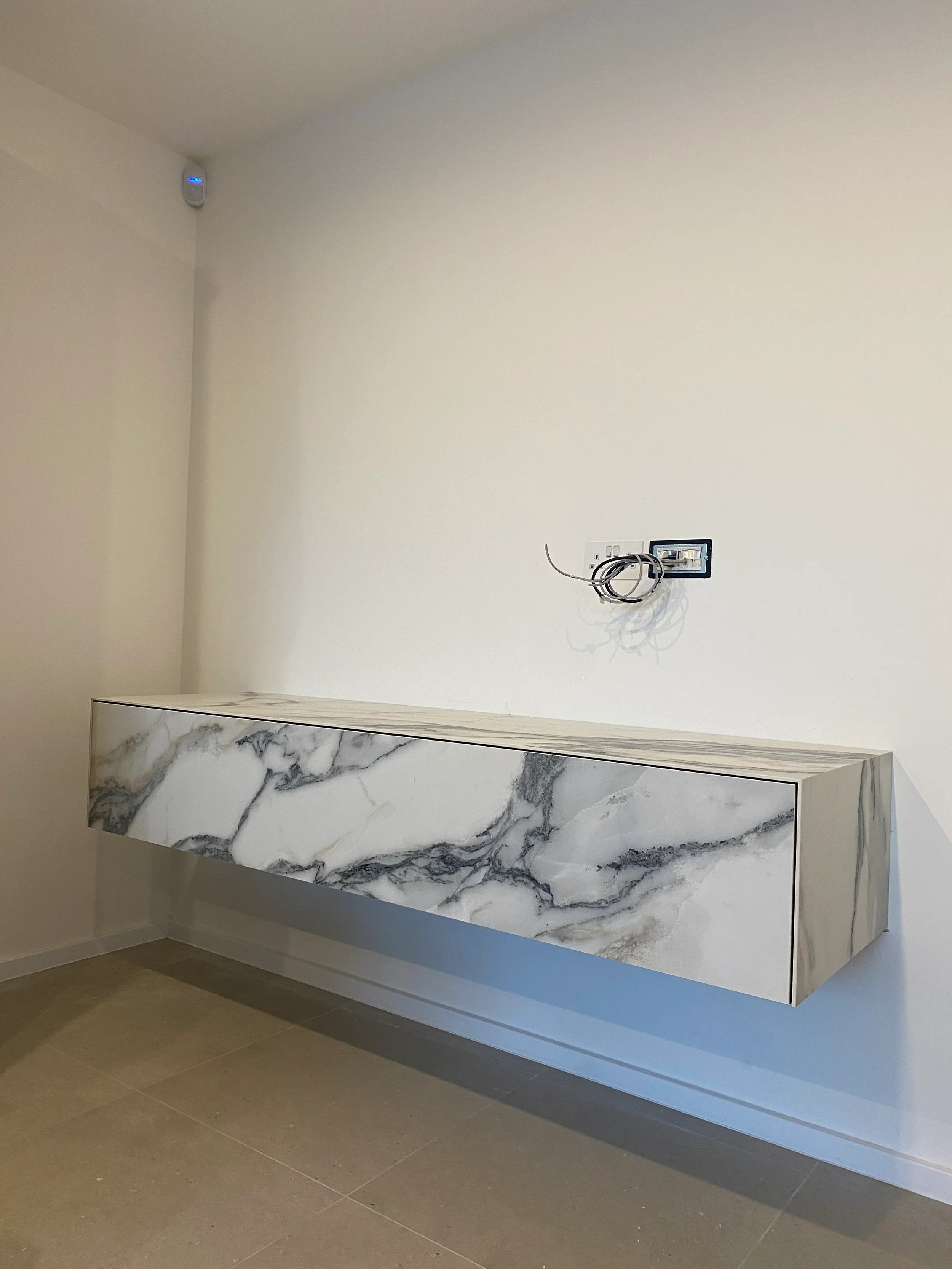 A high-end, minimalist floating wall unit clad in striking, large-format marble-effect porcelain, designed as a sophisticated and seamless storage solution.
