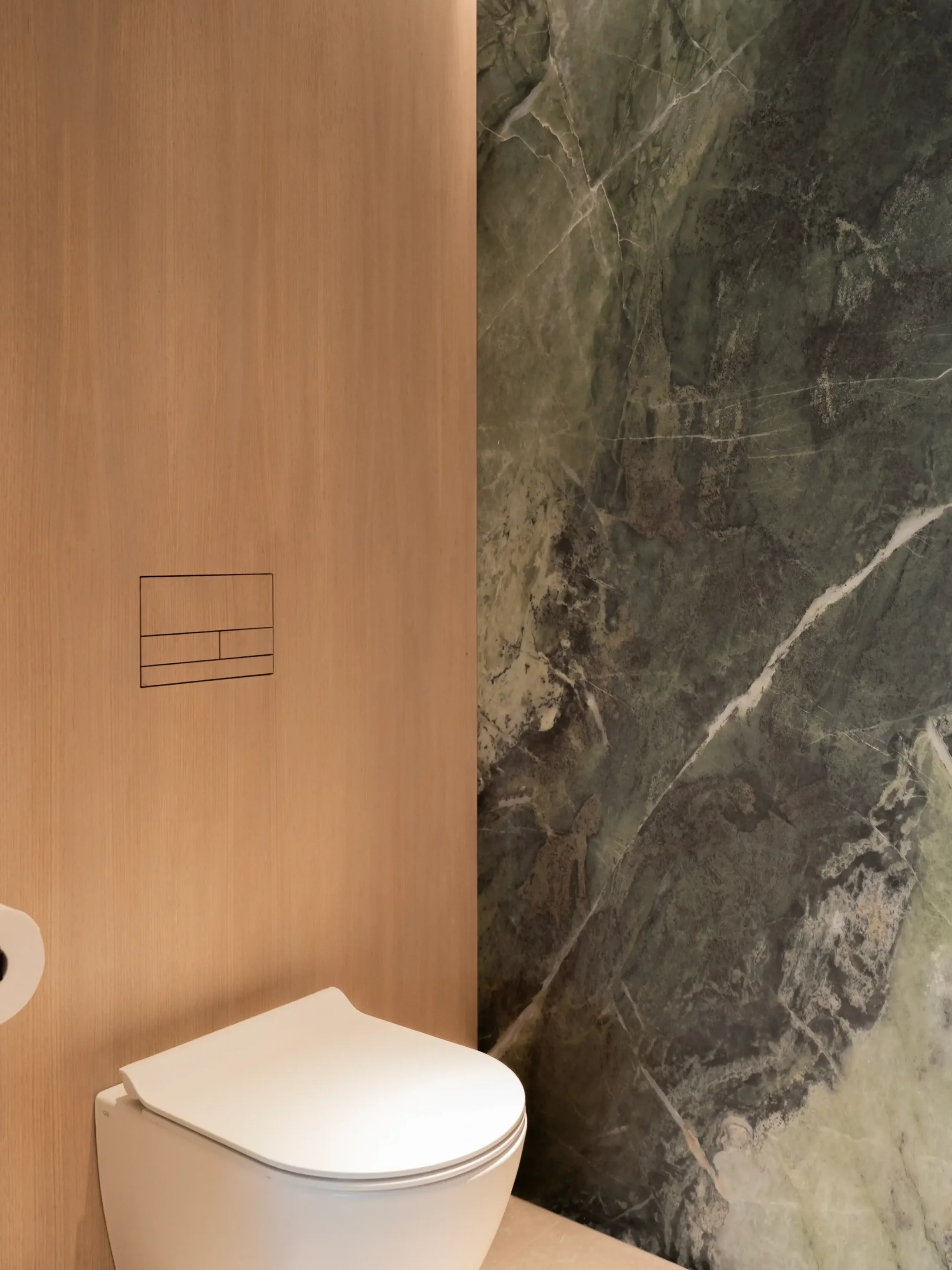 Modern wall-mounted toilet featuring a seamless Clanea veneer flush plate set into wood paneling alongside luxury Florim Heritage Emerald stone-effect porcelain slab wall cladding.