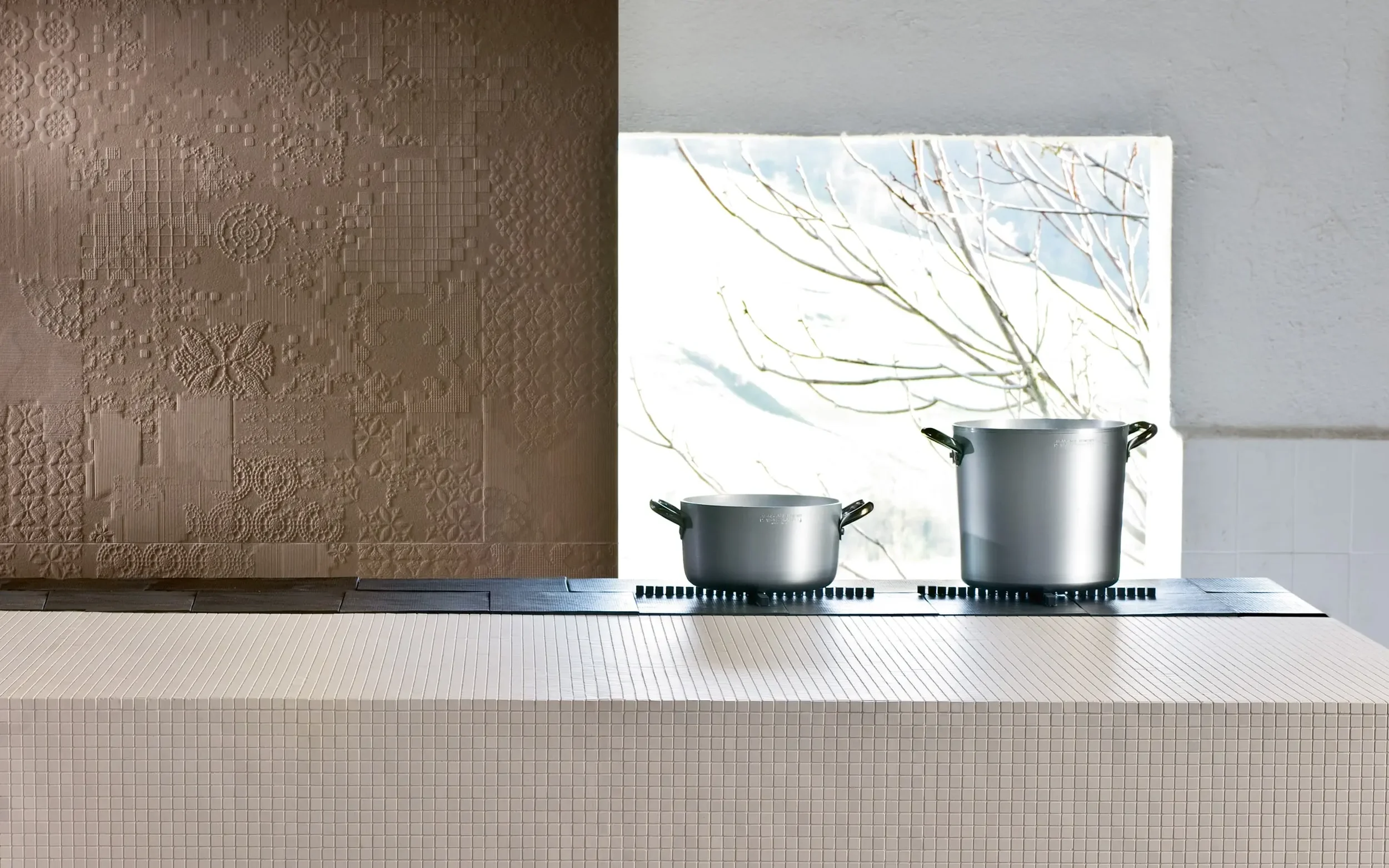 Kitchen interior featuring Mutina porcelain surfaces, including patterned wall cladding and an island wrapped in the Teknotessere collection's minimal 1×1 cm micro-tiles, showcasing PietraCasa's expertise in bespoke installation.