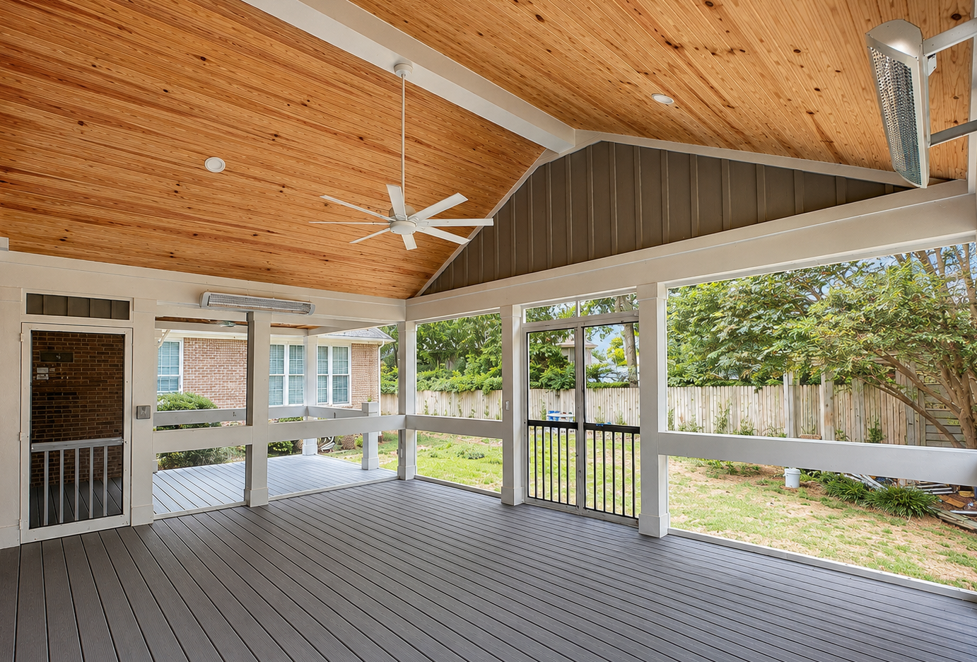 Covered backyard patio with wooden ceiling, ceiling fan, and screened-in railing, overlooking a grassy yard with trees and a wooden fence.