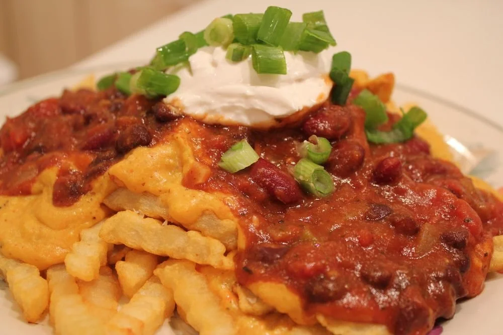 Plate of chili cheese fries topped with sour cream and chopped green onions.