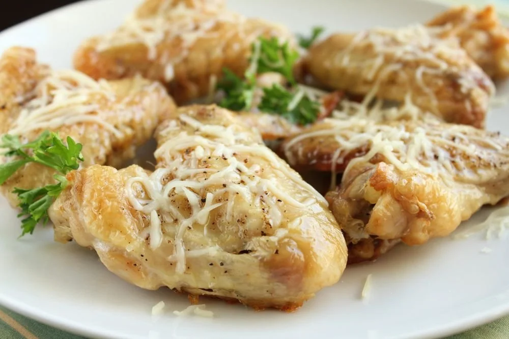 Baked chicken drumsticks topped with shredded cheese and garnished with cilantro on a white plate.