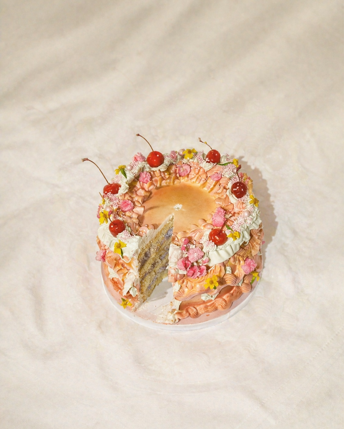 A pink decorated birthday cake with cherries and flowers, with a slice removed showing multiple layers inside.