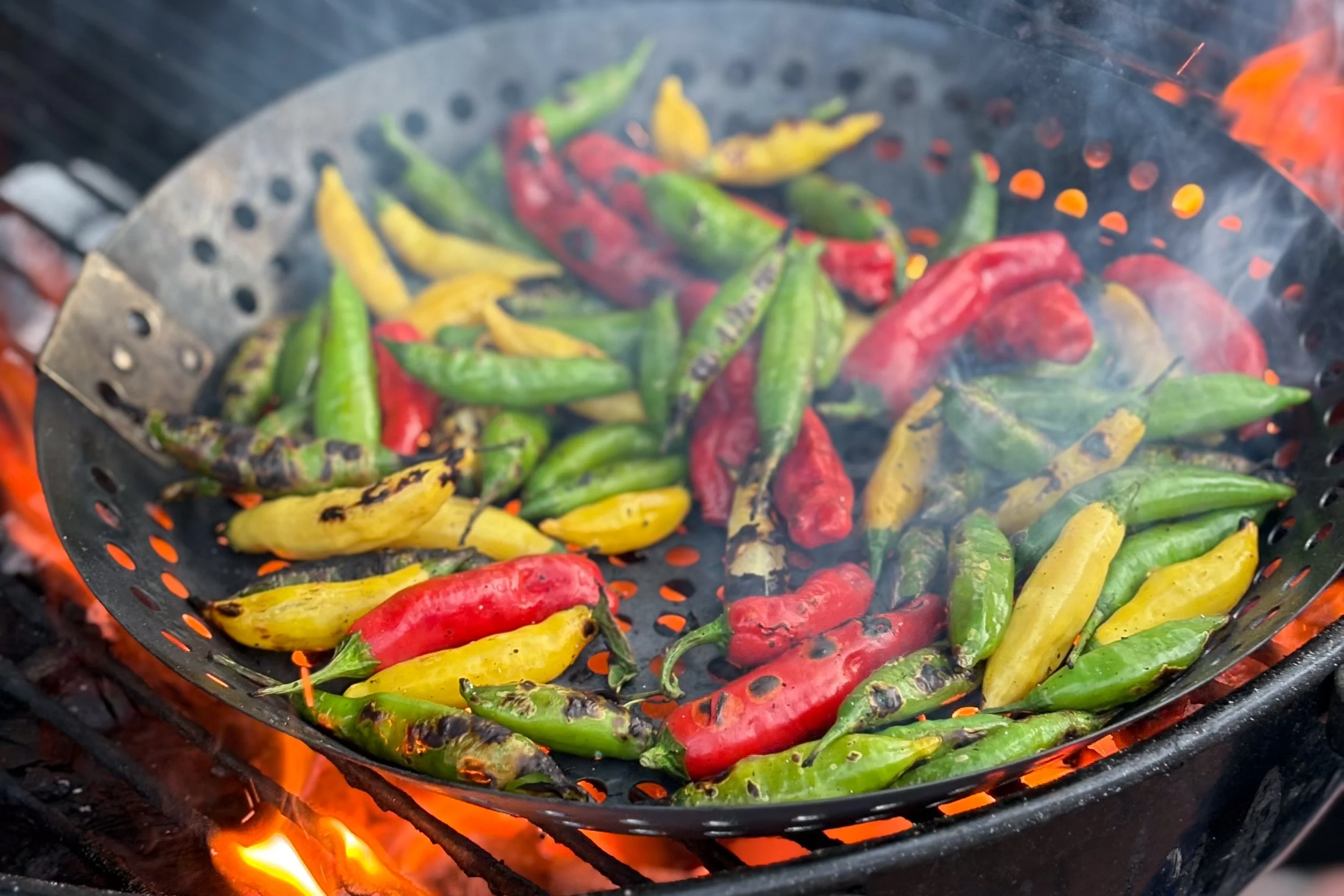 Colorful chili peppers grilling on a barbecue over open flame.