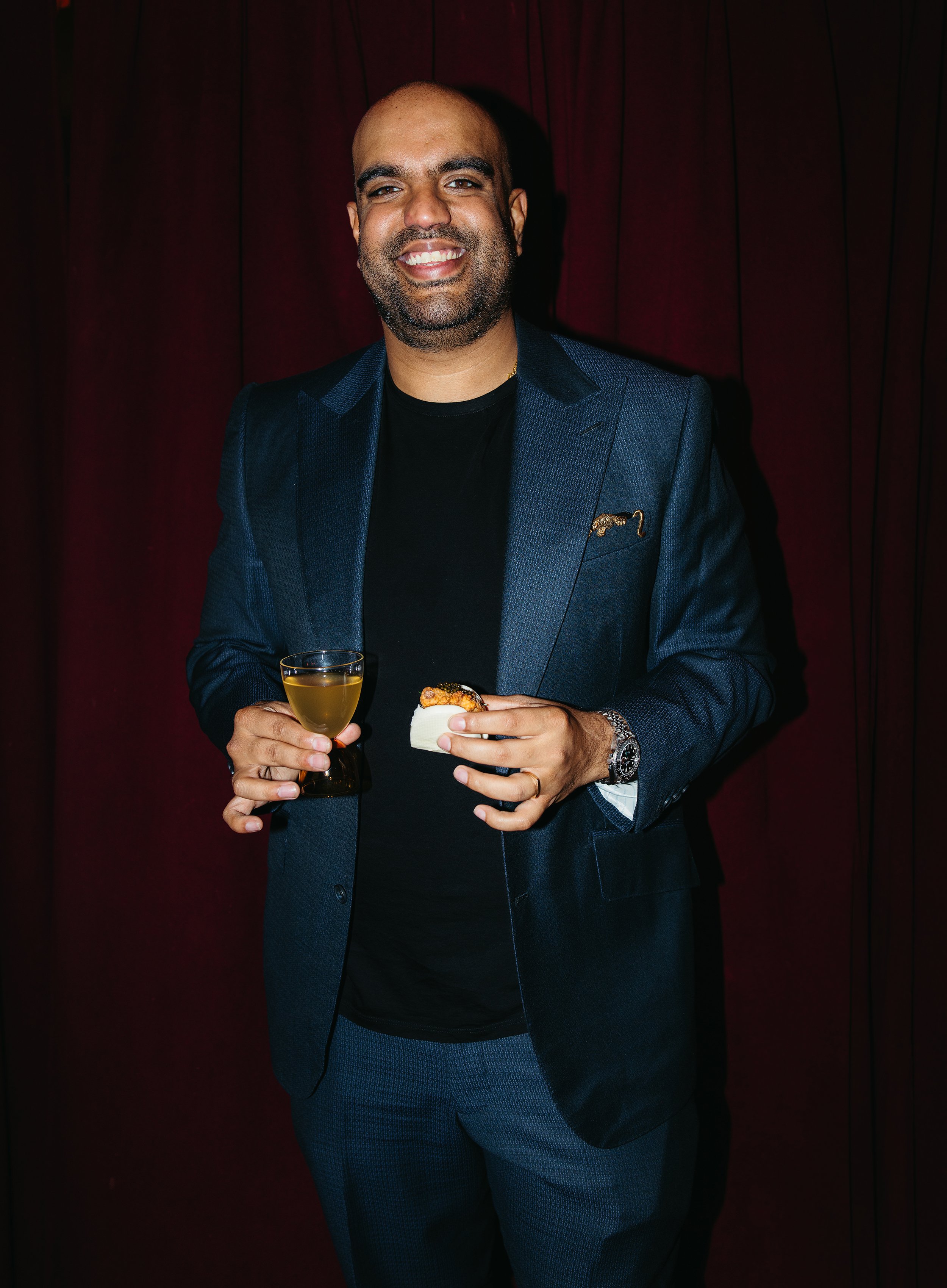 Aly Bandali smiling with a drink and a small plate of food