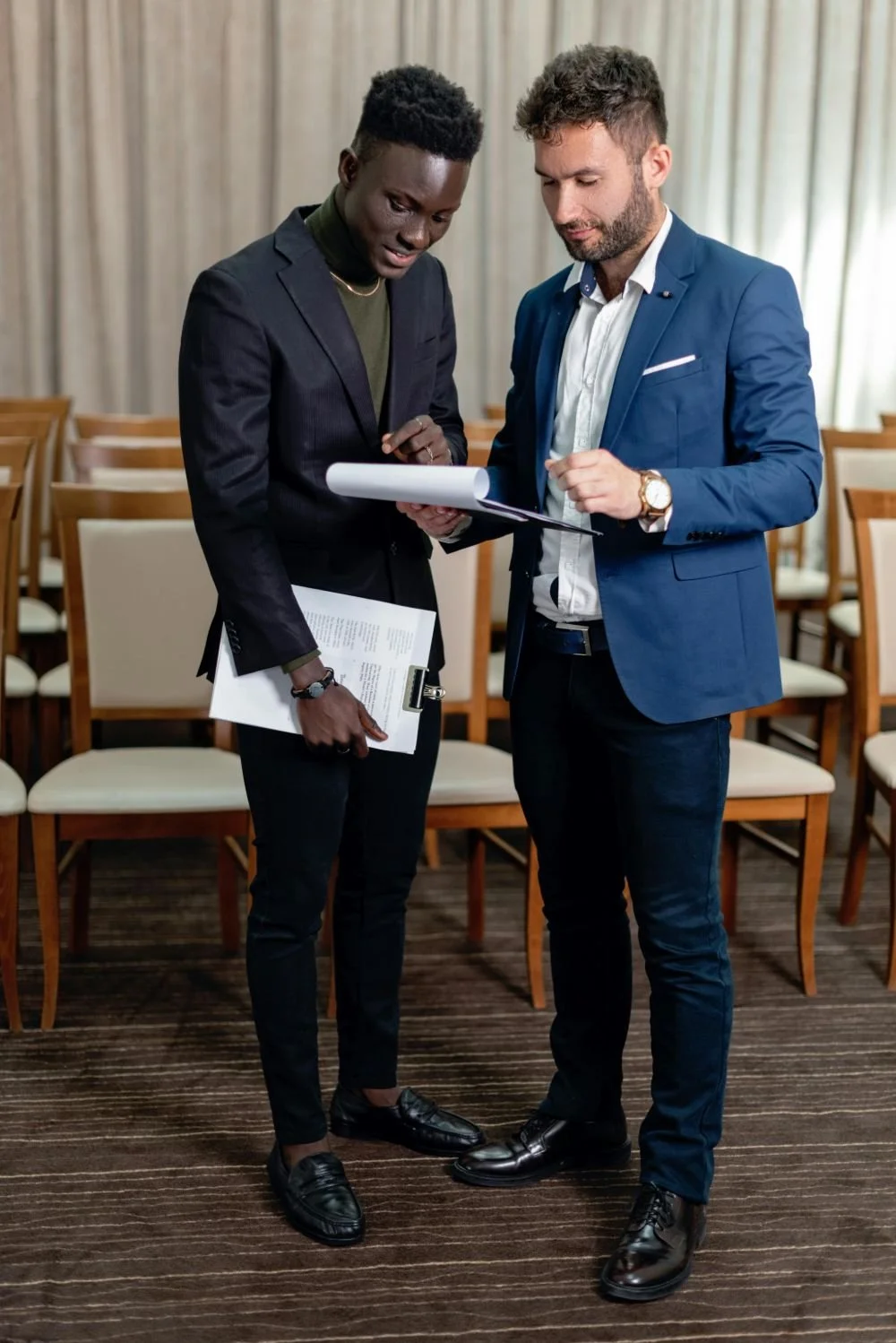 Two business professionals, one black and one white, standing in a conference room, reviewing documents together.