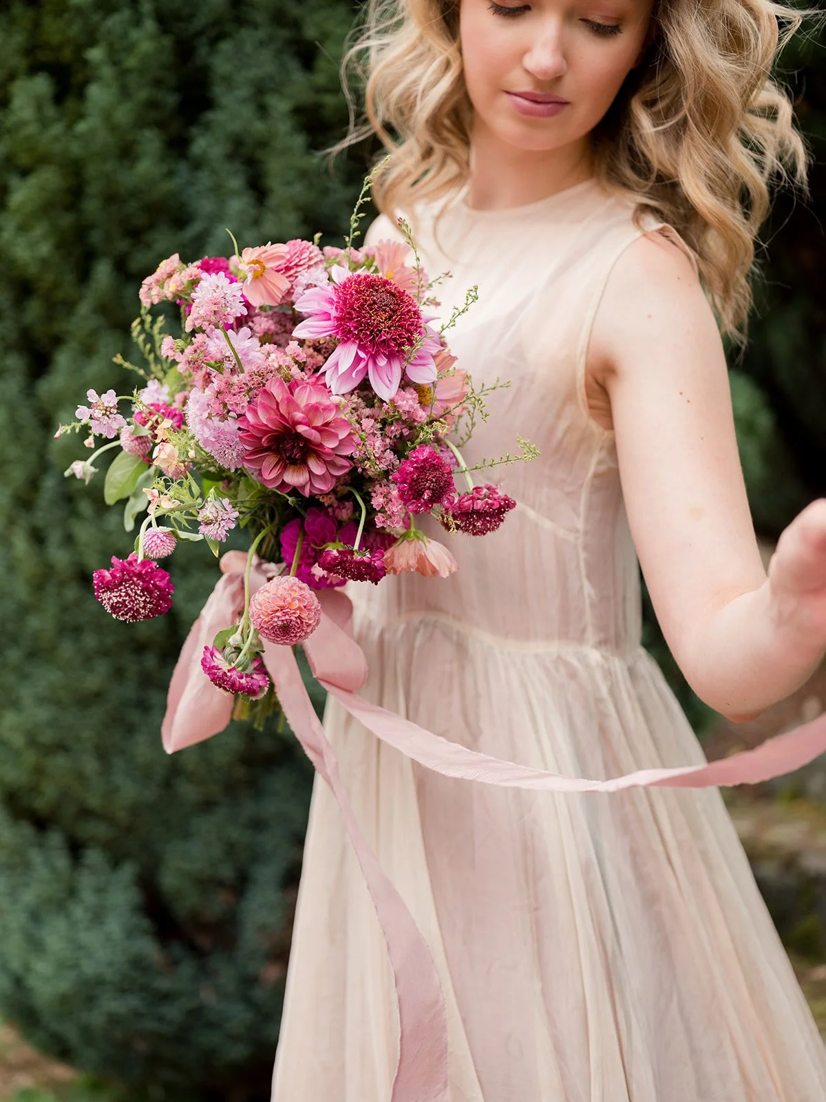 A woman in a light pink dress holding a bouquet of pink flowers outdoors.