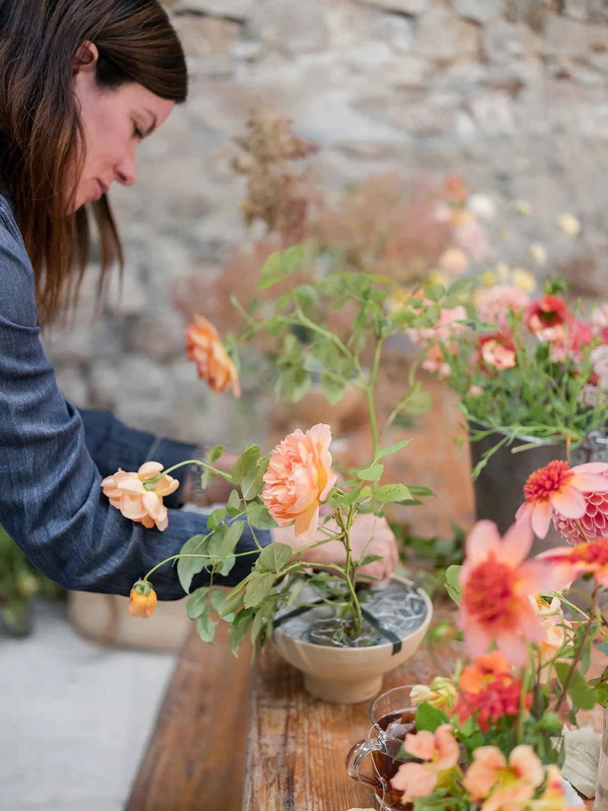Becky Porter arranging pink and orange flowers in a vase at a flower shop or garden center.
