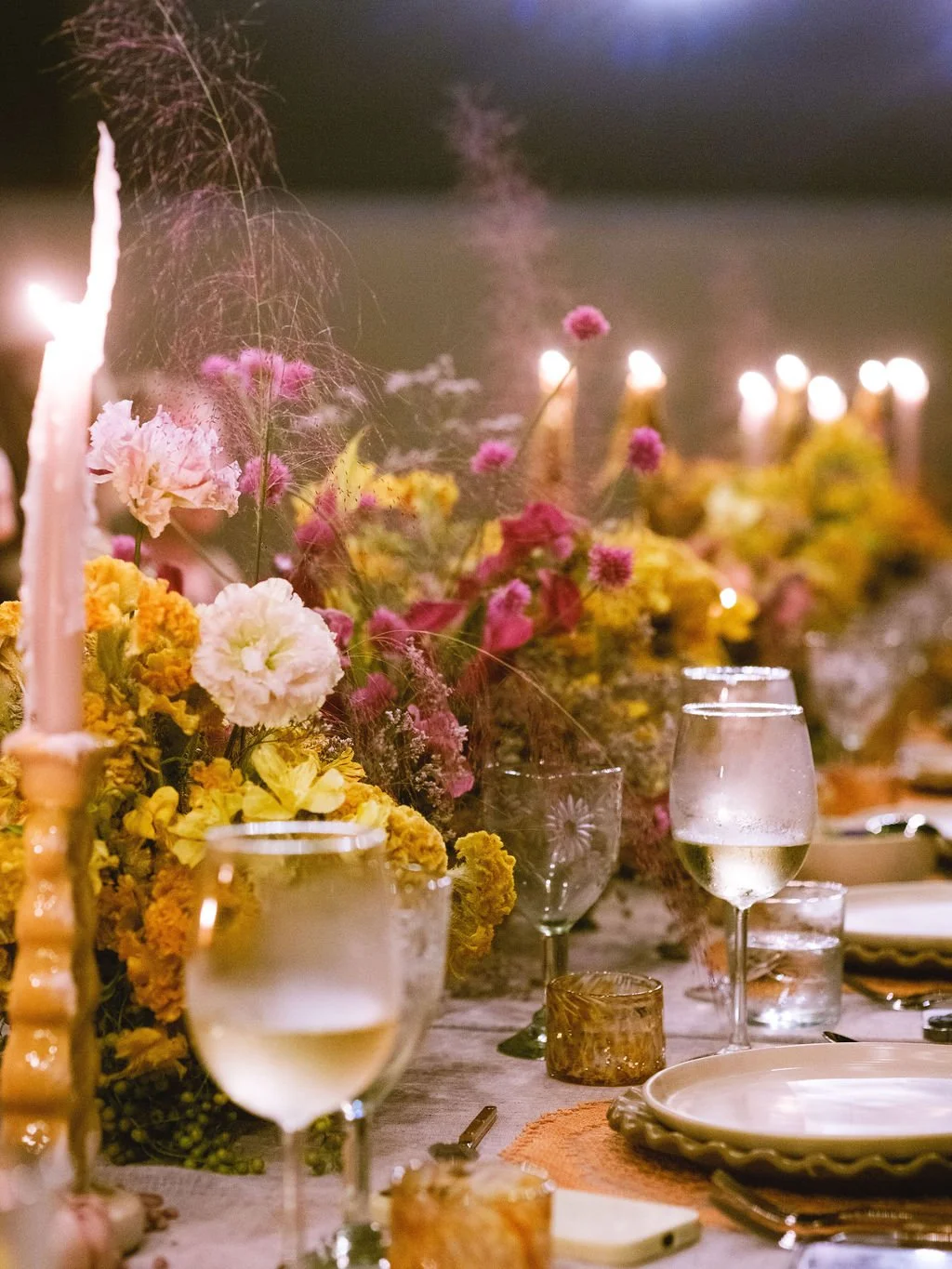 A table decorated with colorful flowers, candles, and glassware, set for a celebration or dinner event.
