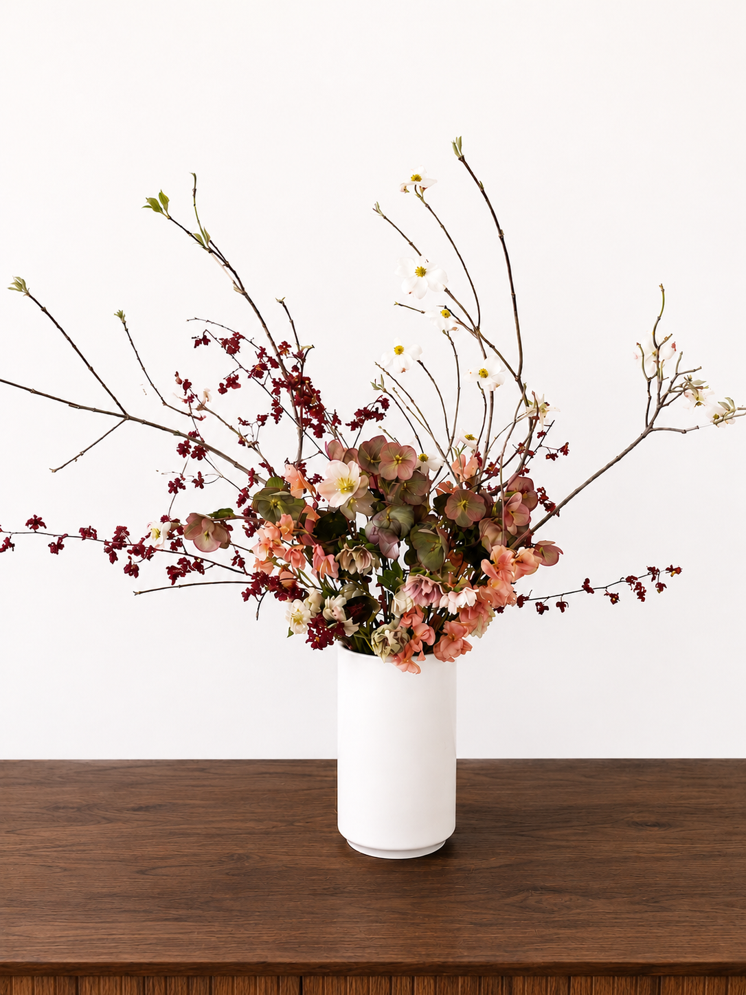 A  Statement Arrangment in a white vase with an arrangement of branches and flowers on a wooden table against a plain white background in Marin County.