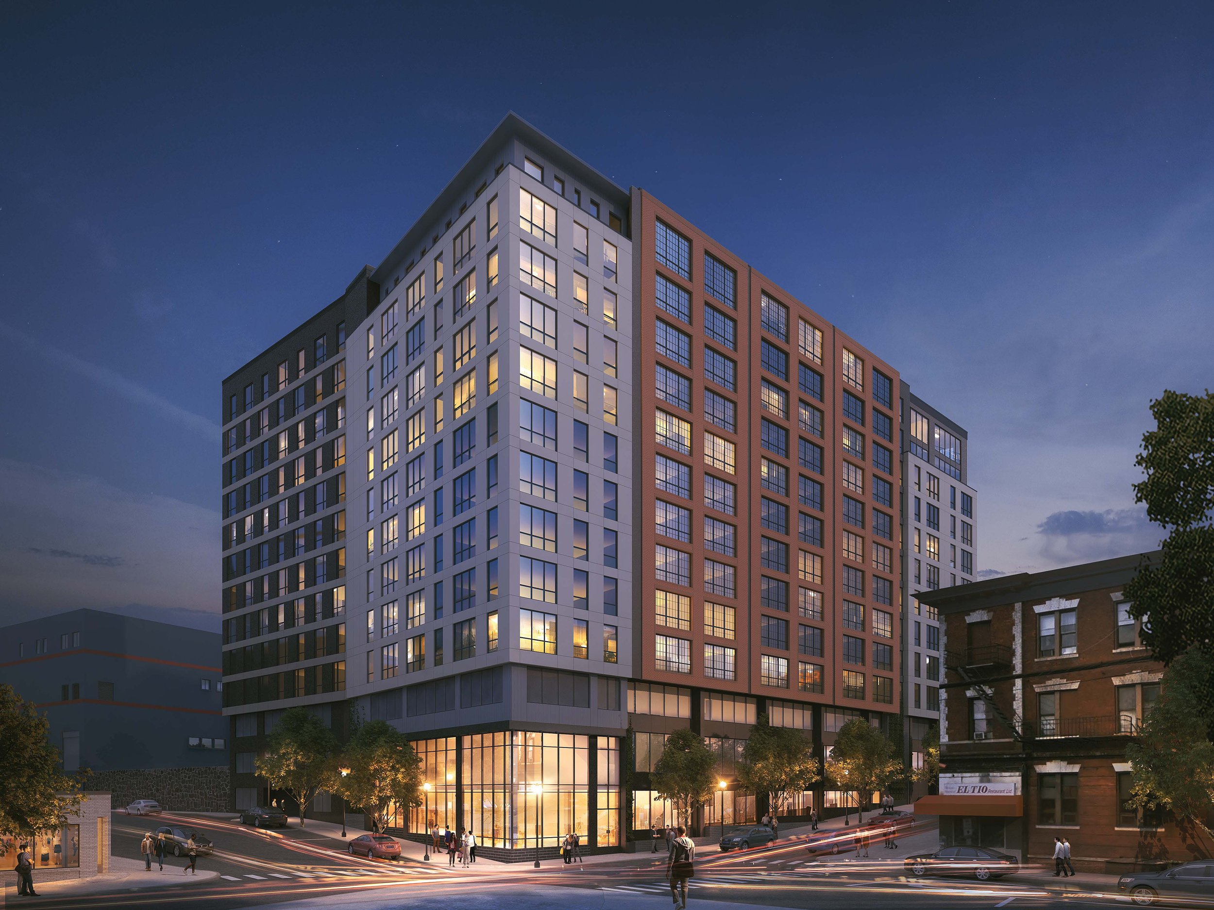 A modern multi-story building at dusk with illuminated windows and trees at the base.