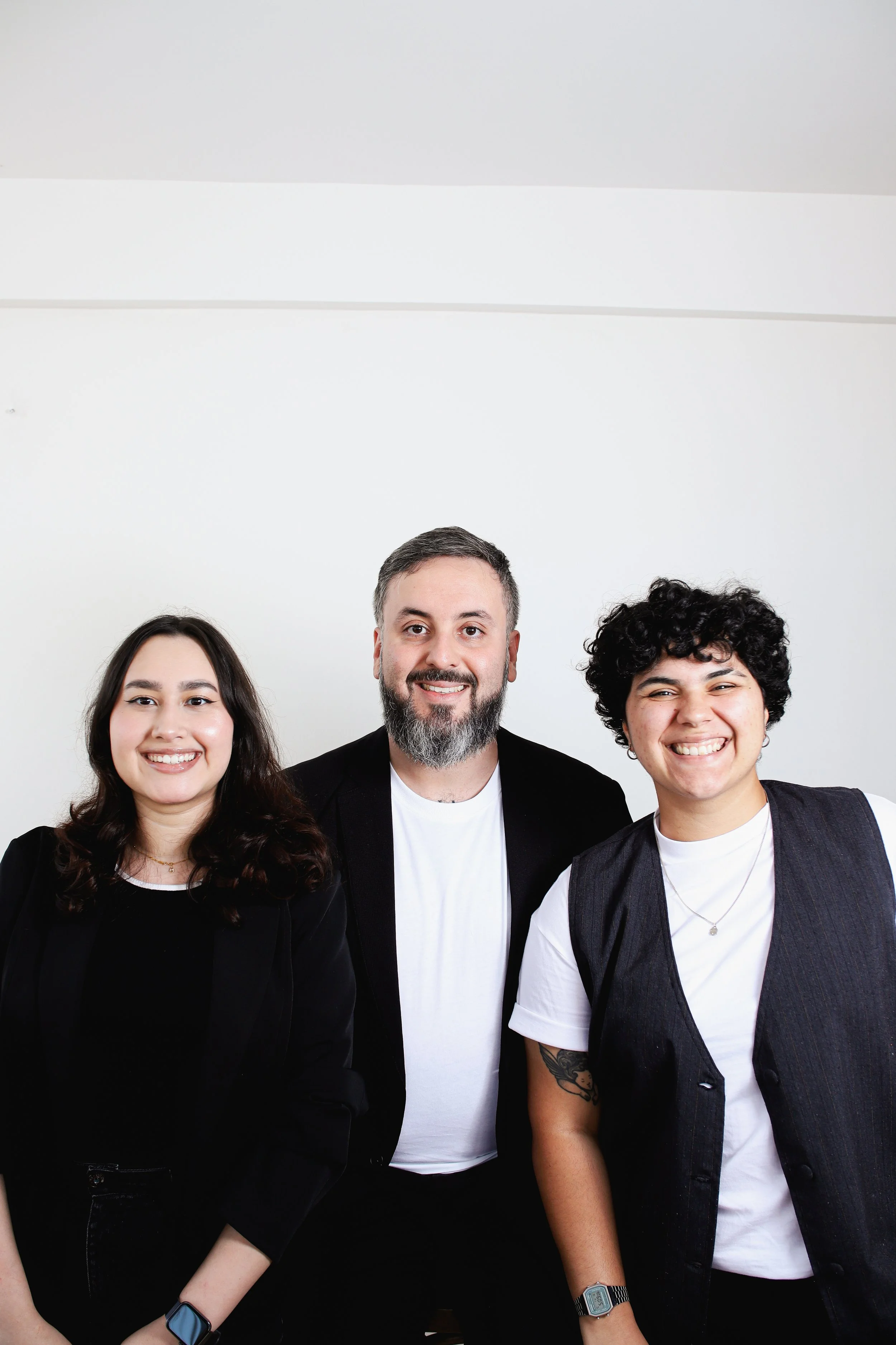 Grupo de quatro pessoas sorrindo à frente de uma parede branca, vestindo roupas casuais e acessórios modernos.