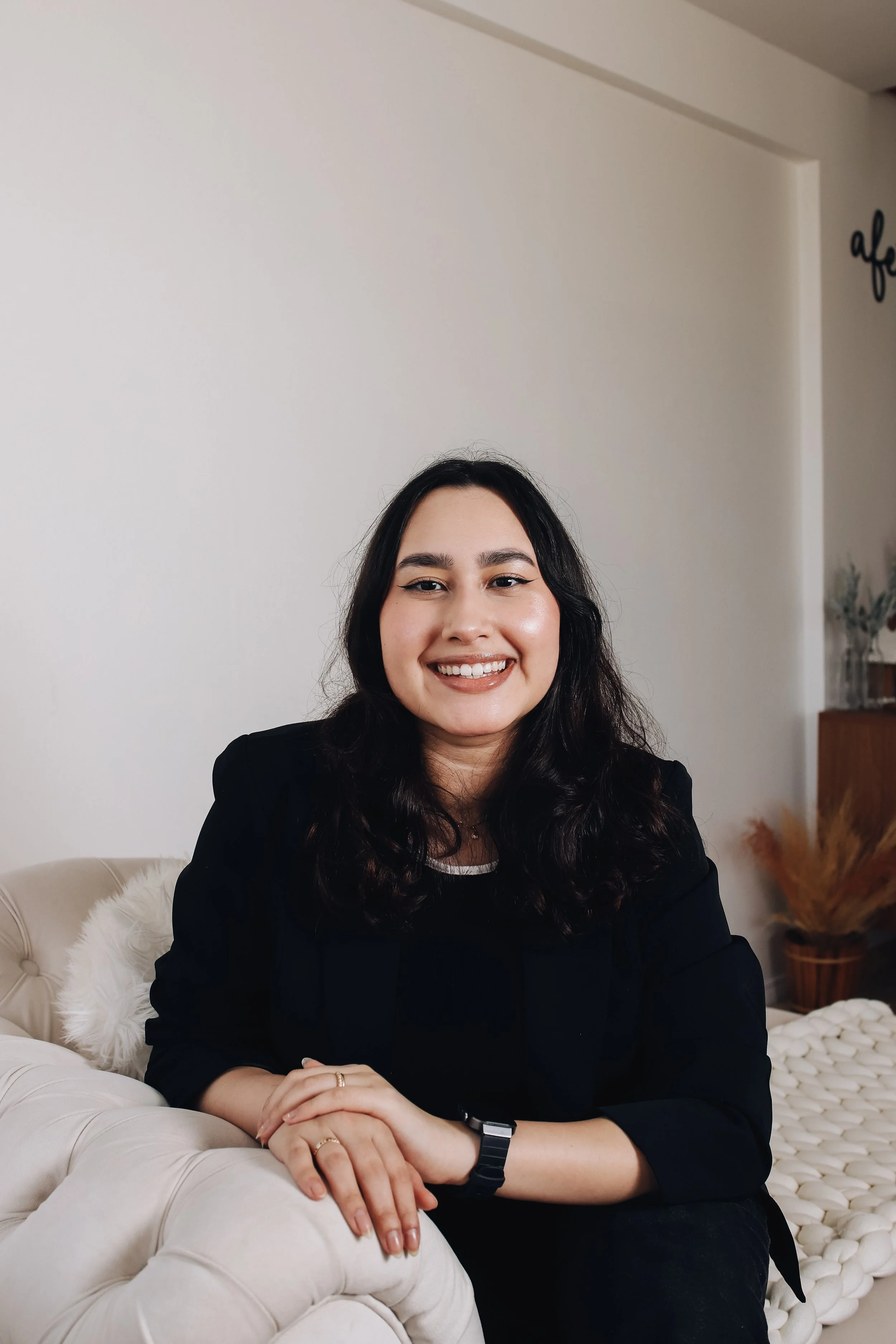 Mulher sorrindo sentado em um sofá com fundo claro e decoração de casa.