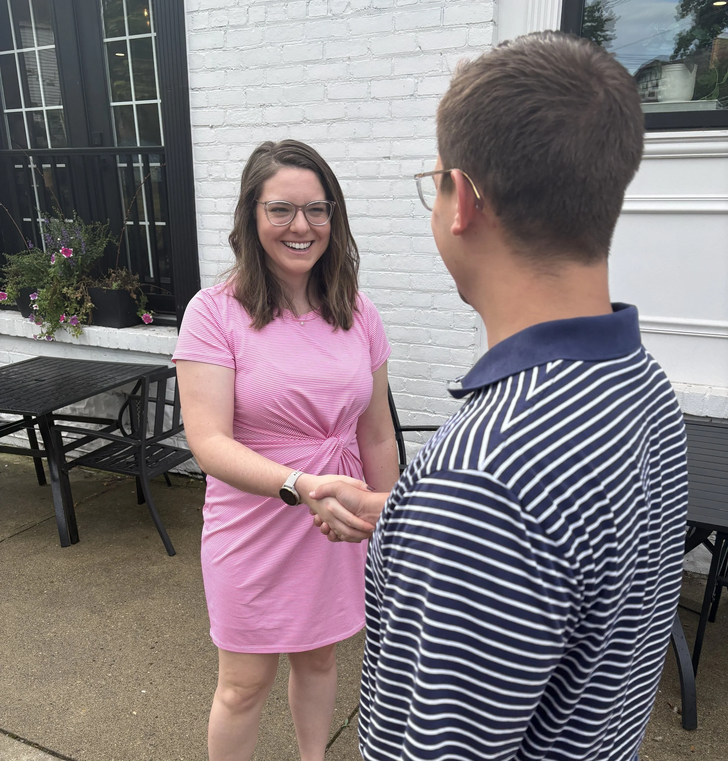 woman in pink dress shaking hands with man in blue striped polo