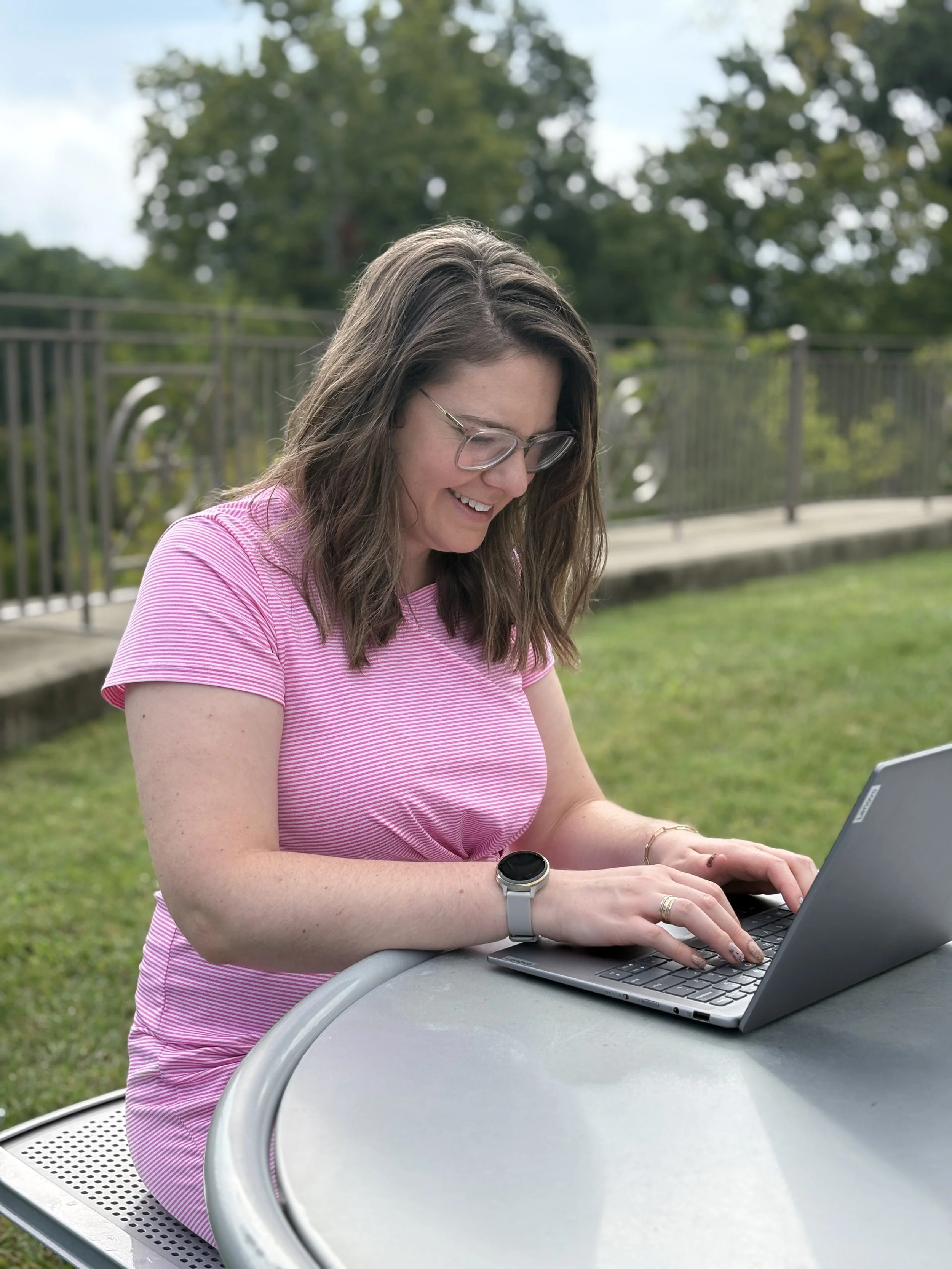 woman in pink dress working on laptop outside